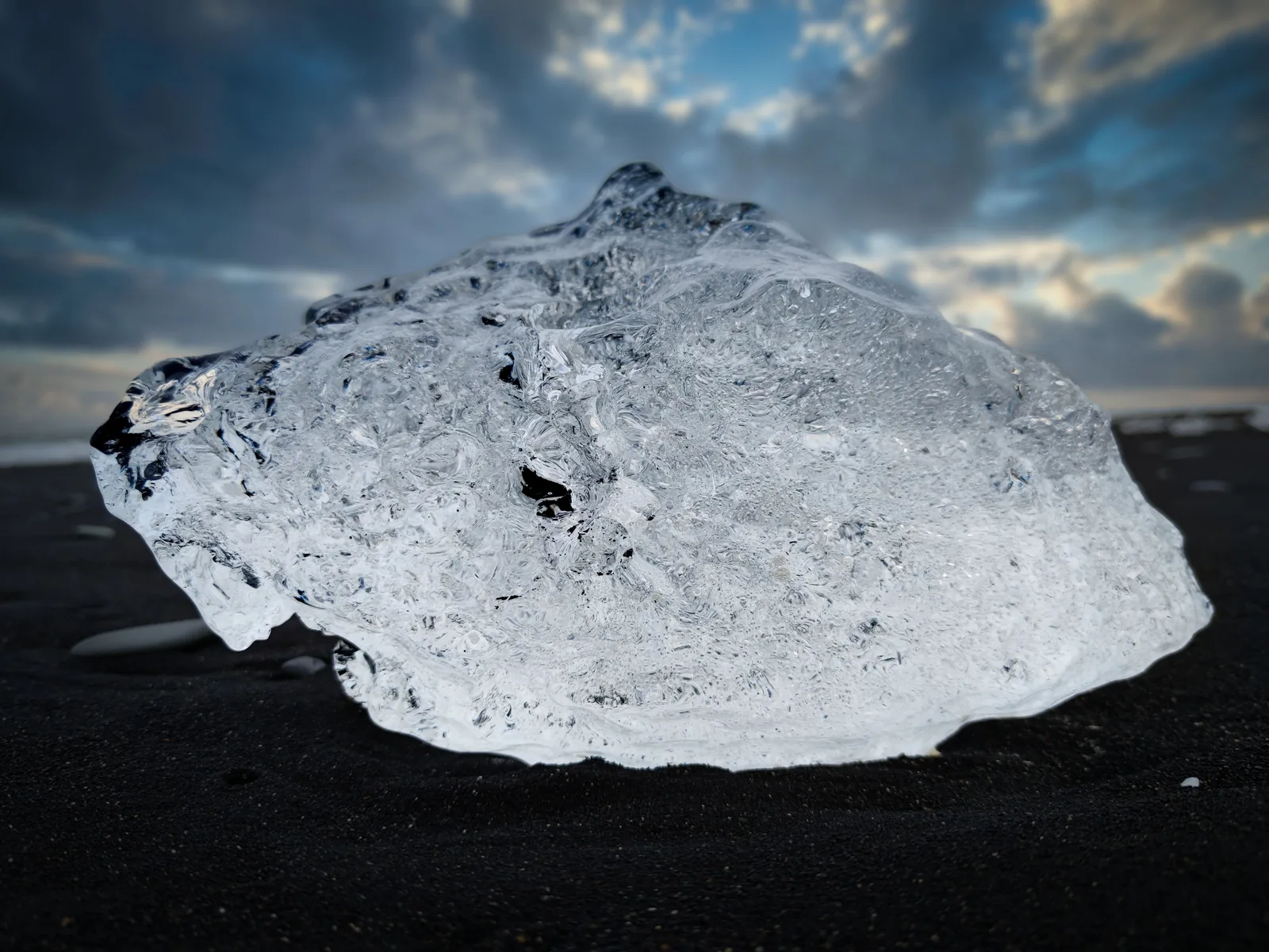 A large block of clear ice sitting on the black sand of Diamond Beach