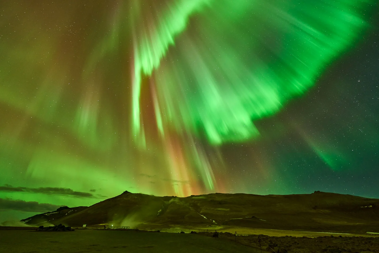 Green northern lights filling the sky over a dark Icelandic landscape