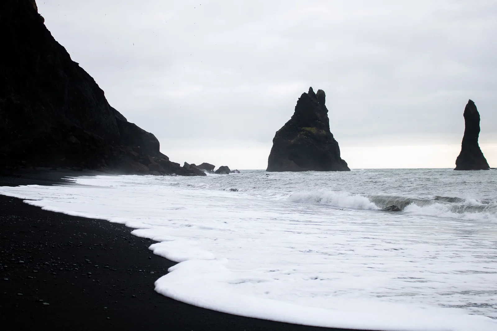A wave running up the black sand at Reynisfjara with the sea stacks offshore