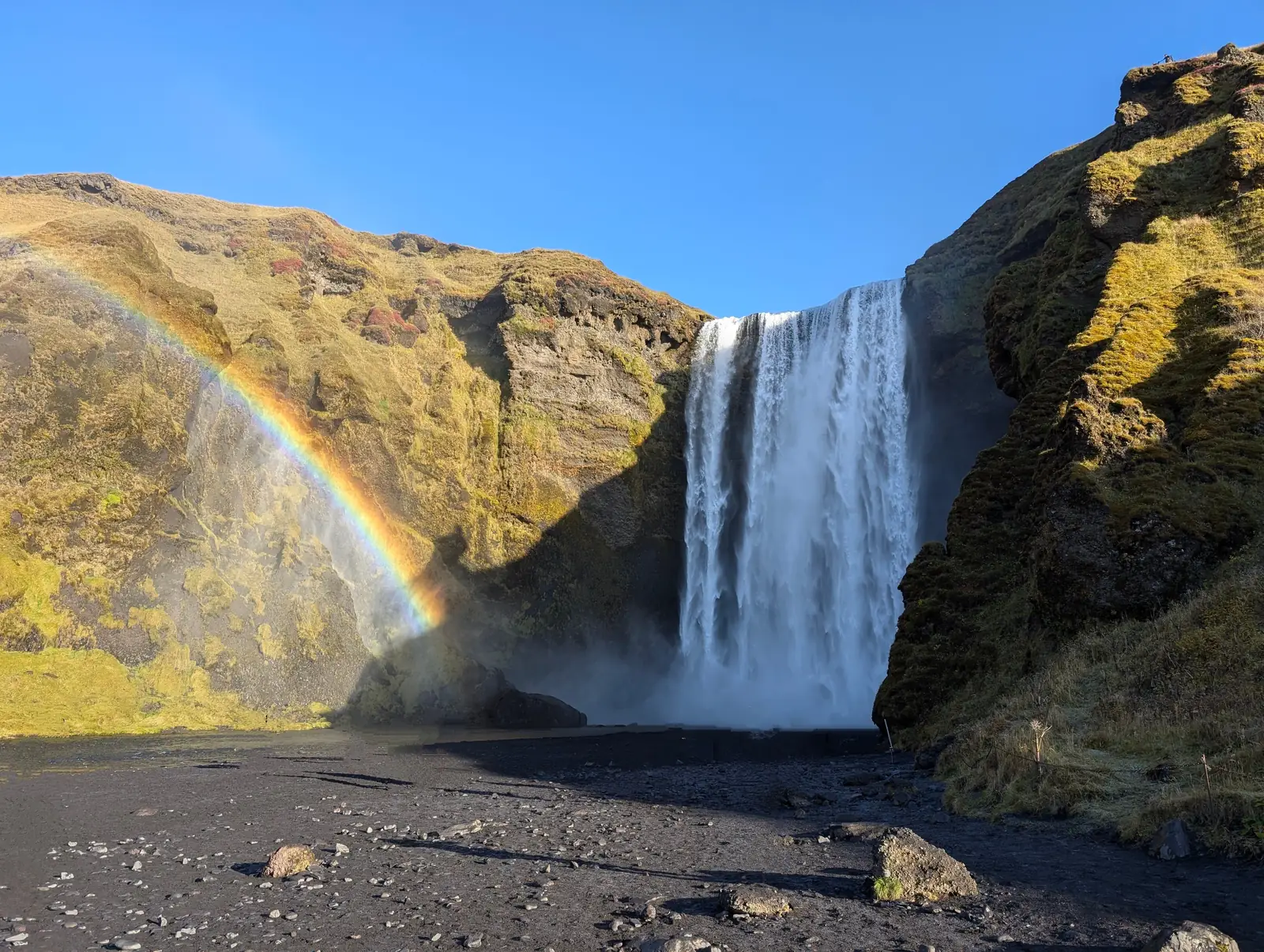 A rainbow across the wide curtain of Skogafoss waterfall under a blue sky