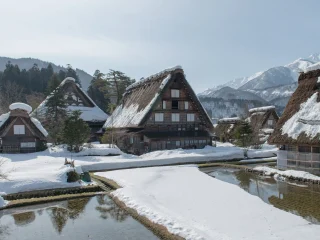 Thatched farmhouses at Shirakawa Go under snow with mountains behind