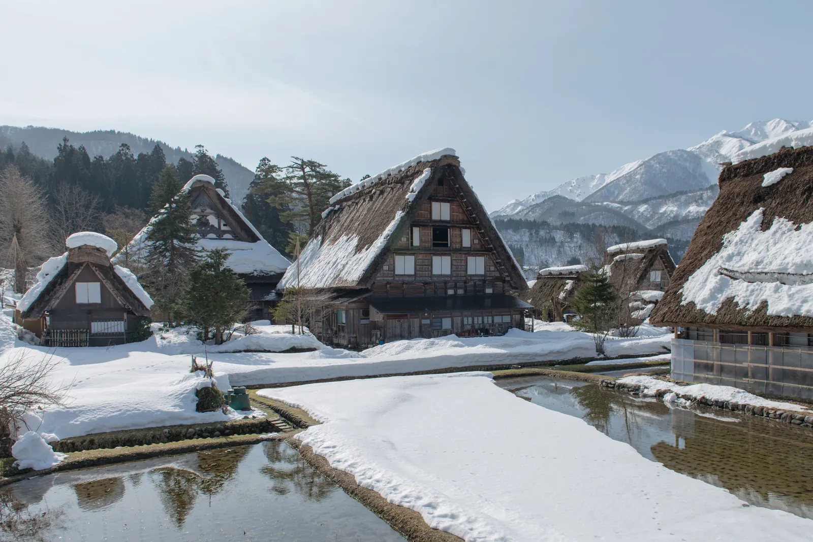 Thatched farmhouses at Shirakawa Go under snow with mountains behind