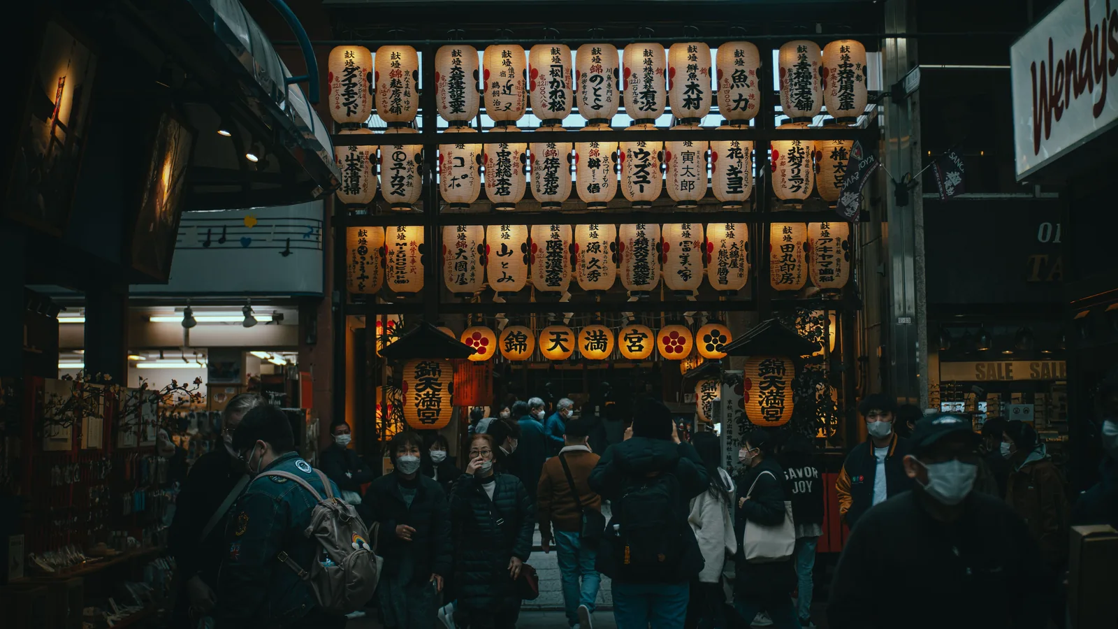 Rows of paper lanterns above shoppers in a covered market street in Kyoto