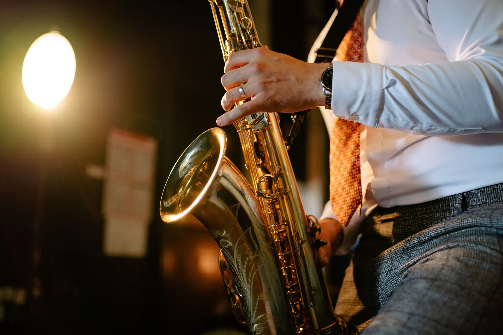 A close view of hands on a saxophone under a warm stage light