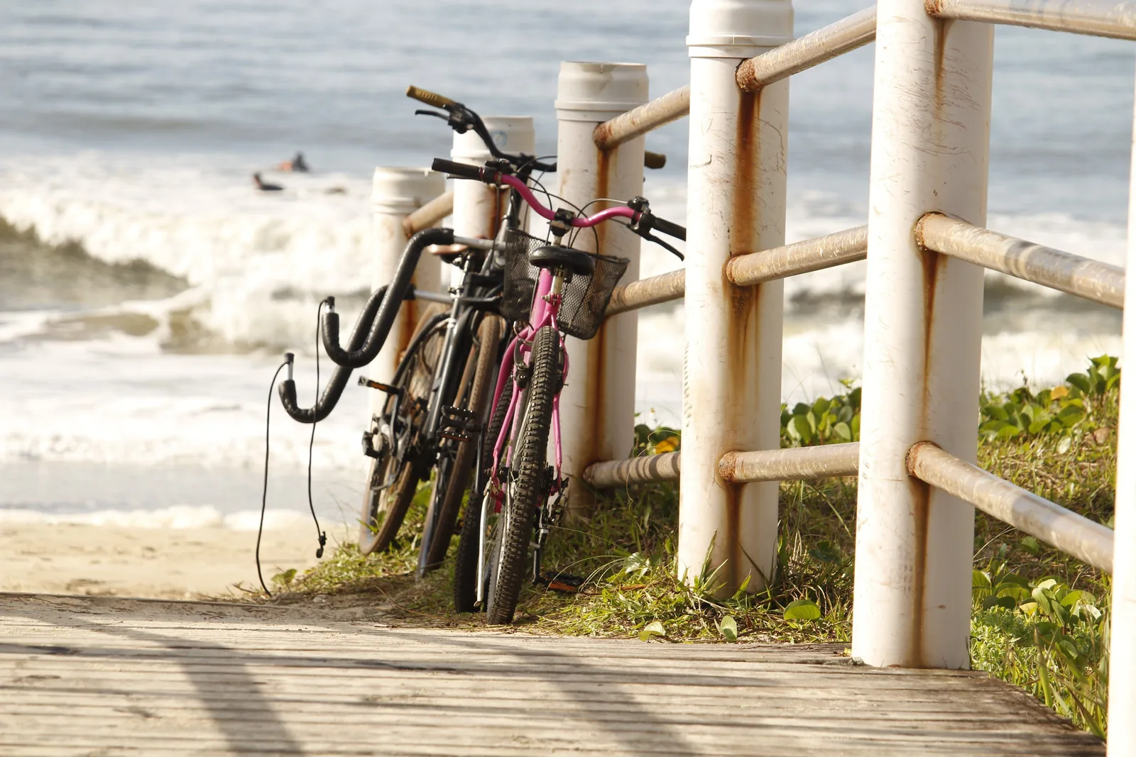 Two bicycles leaning against a railing on a paved path beside the ocean