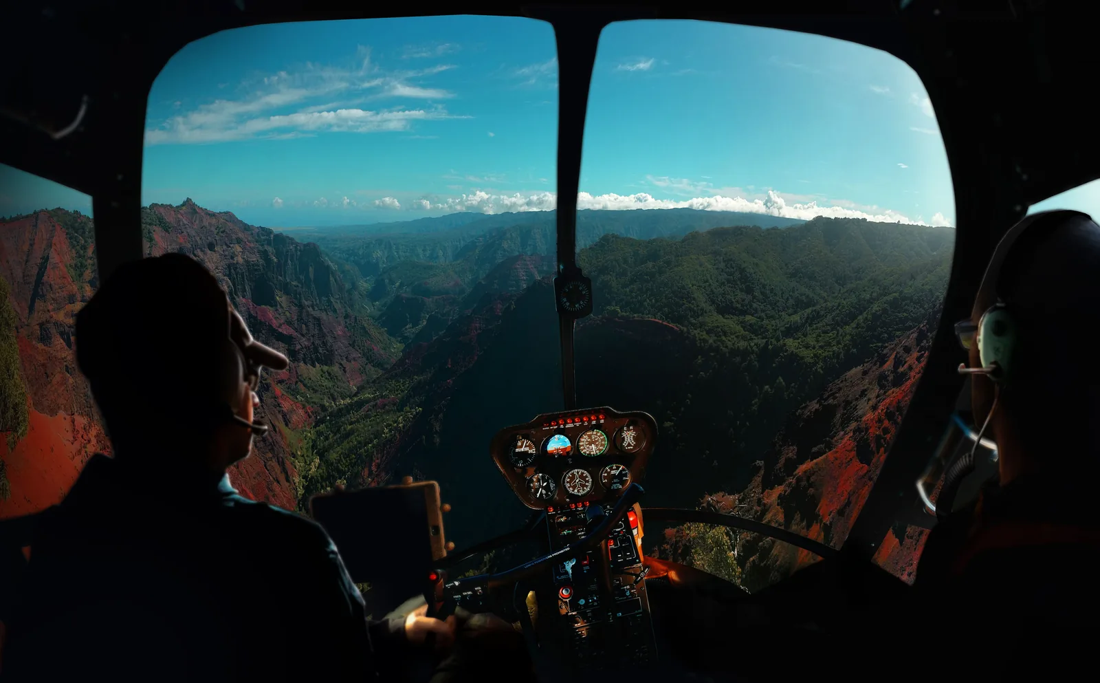 The view out of a helicopter cockpit over a deep red canyon