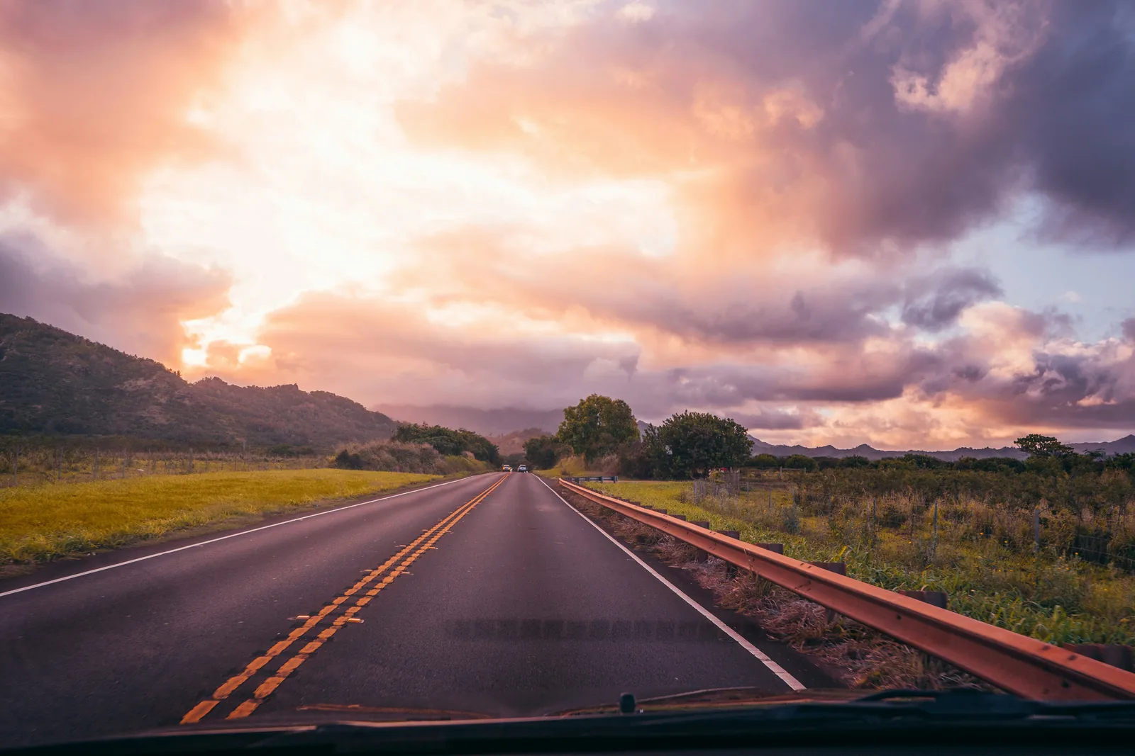 The view down an empty road through the windshield at sunset
