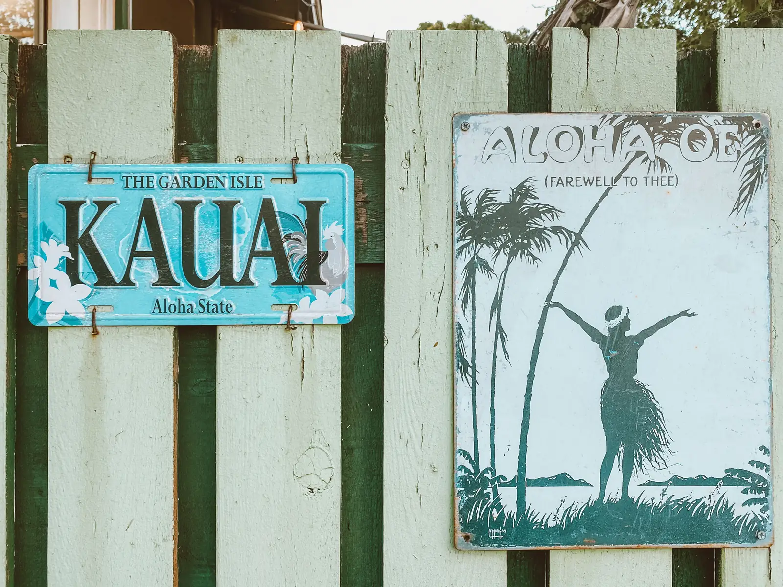 A Kauai sign and an old Aloha plate hanging on a weathered wooden fence