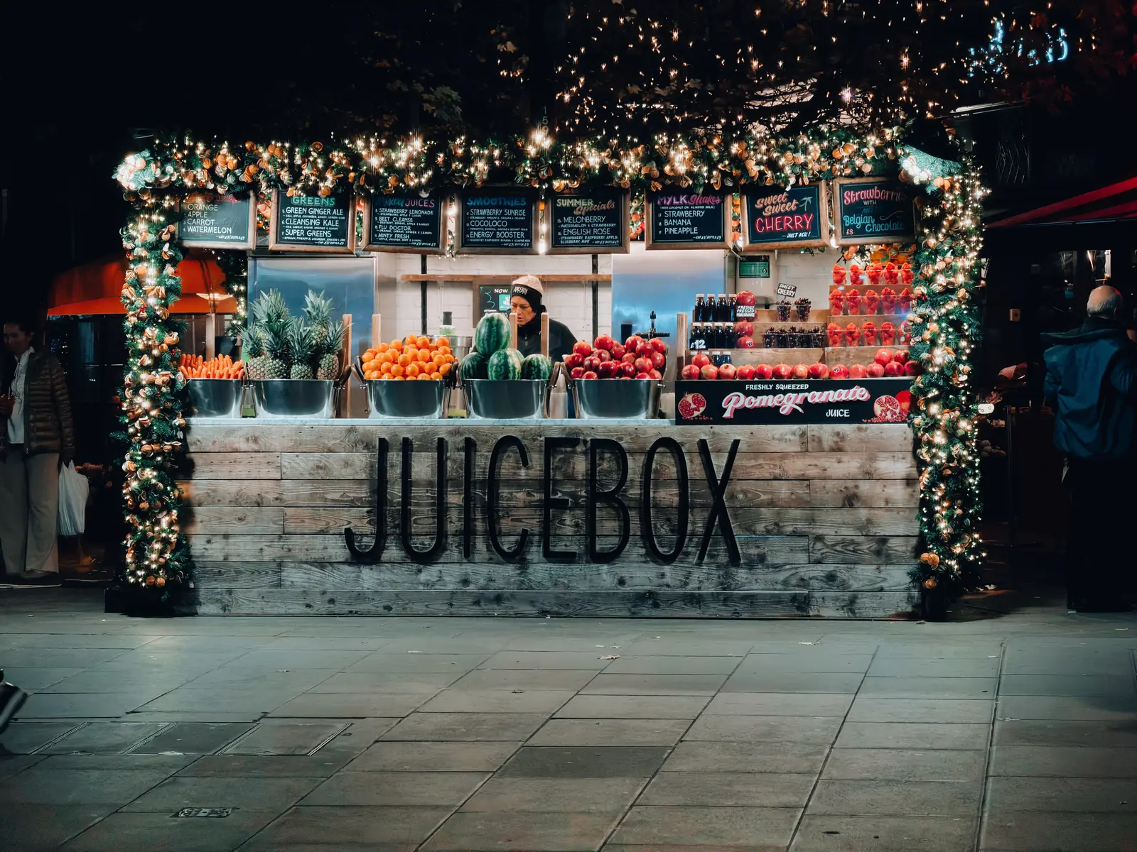 A festive drinks stand lit up on a London street at night