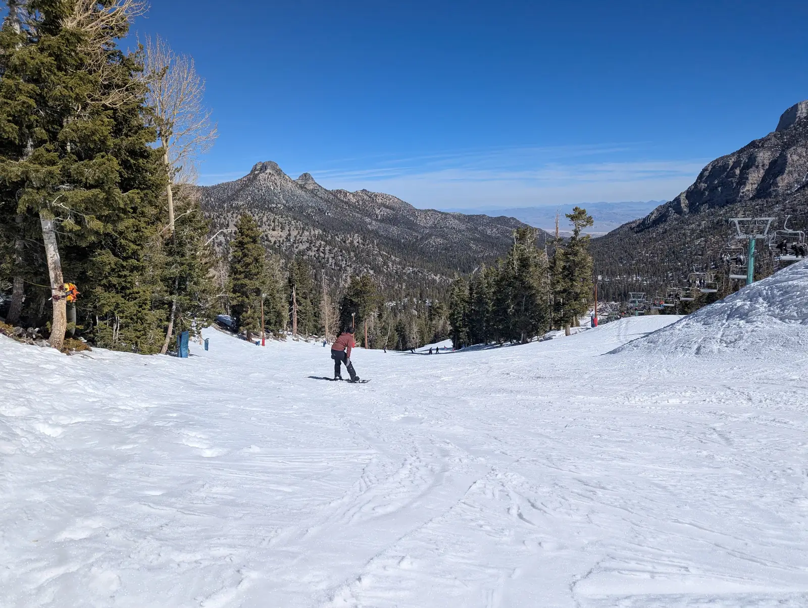 A snowy run lined with pines on Mount Charleston with desert peaks beyond