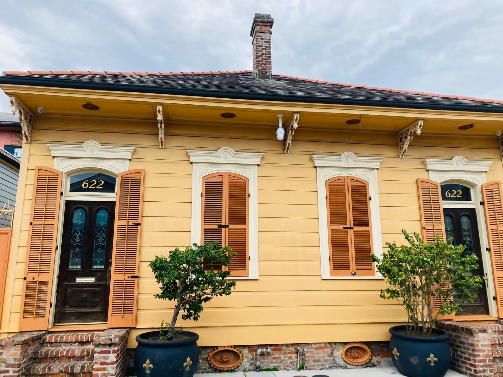 A yellow Creole cottage with orange shutters and fleur de lis planters in New Orleans