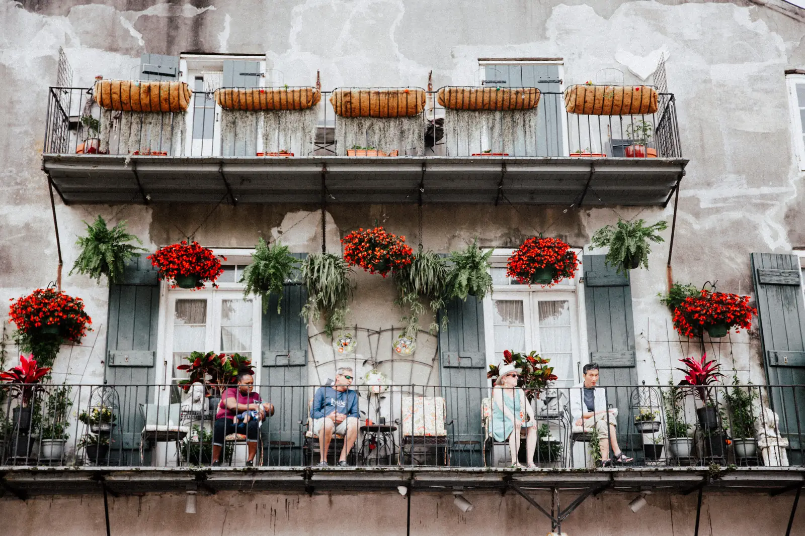 People sitting out on a French Quarter balcony crowded with ferns and hanging flowers