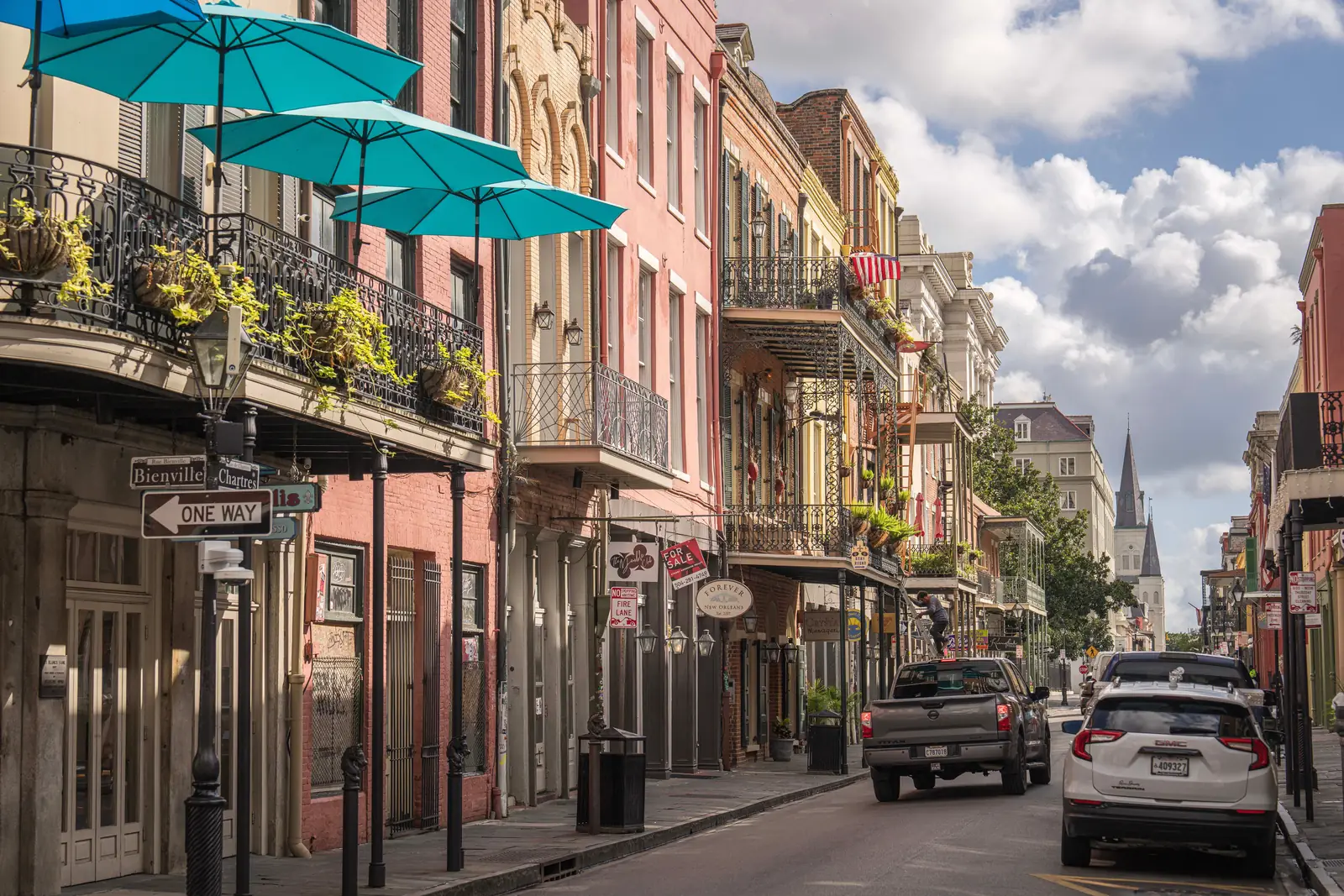 Iron balconies and pastel buildings along a French Quarter street with the cathedral spire beyond