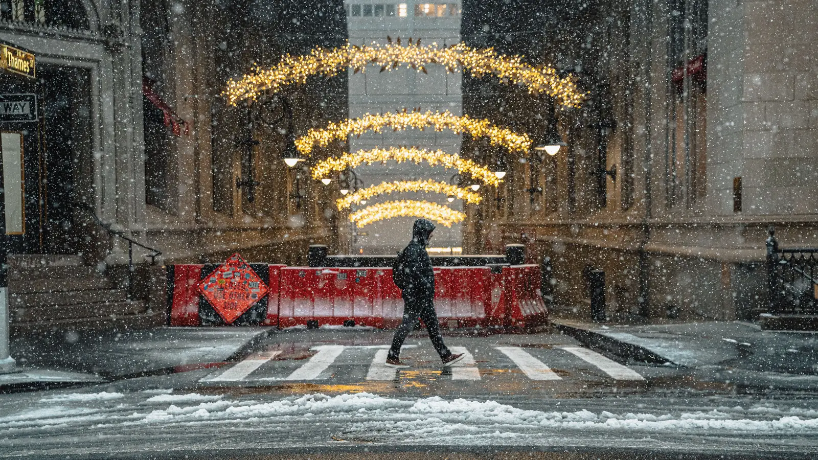 Snow falling on a New York street under strings of golden holiday lights