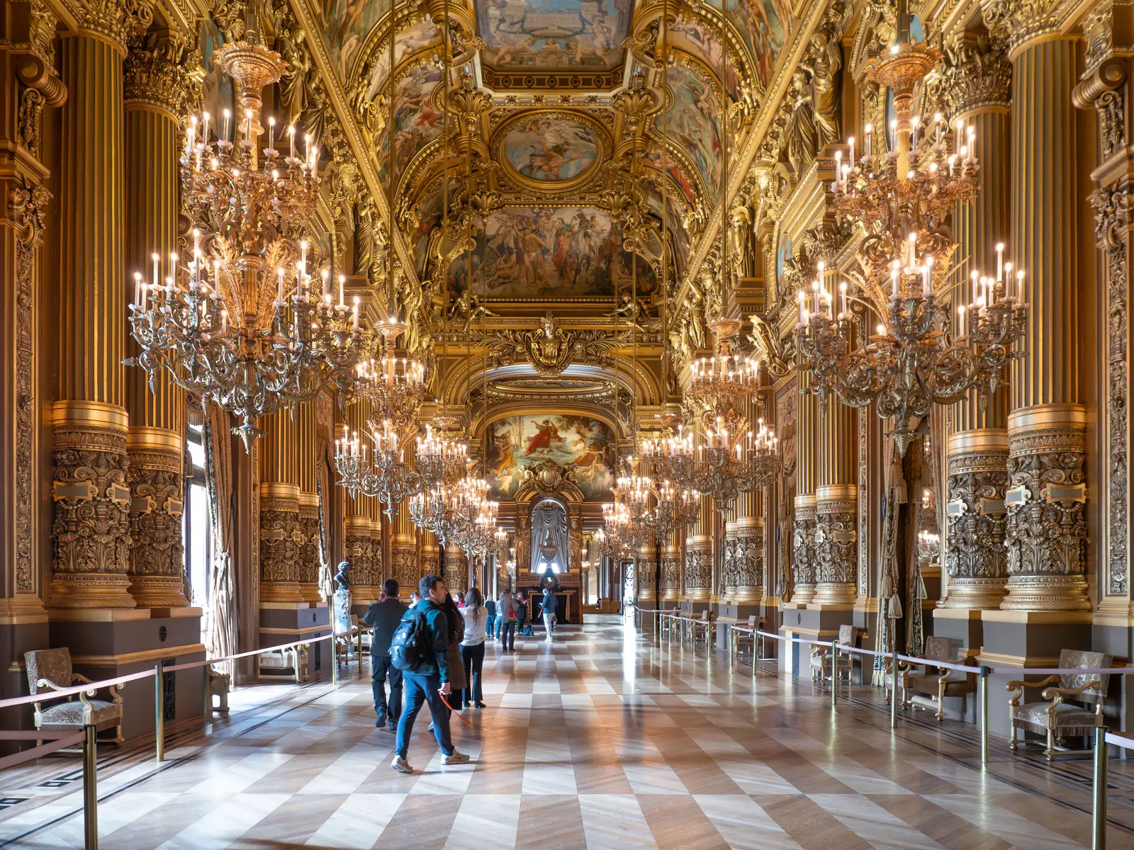 The Grand Foyer of the Palais Garnier in Paris lined with chandeliers and gilded columns