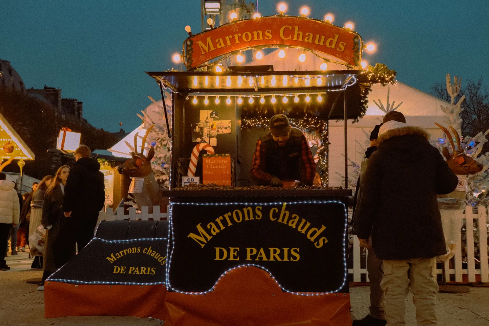 A hot chestnut stall lit up at a Christmas market in Paris after dark