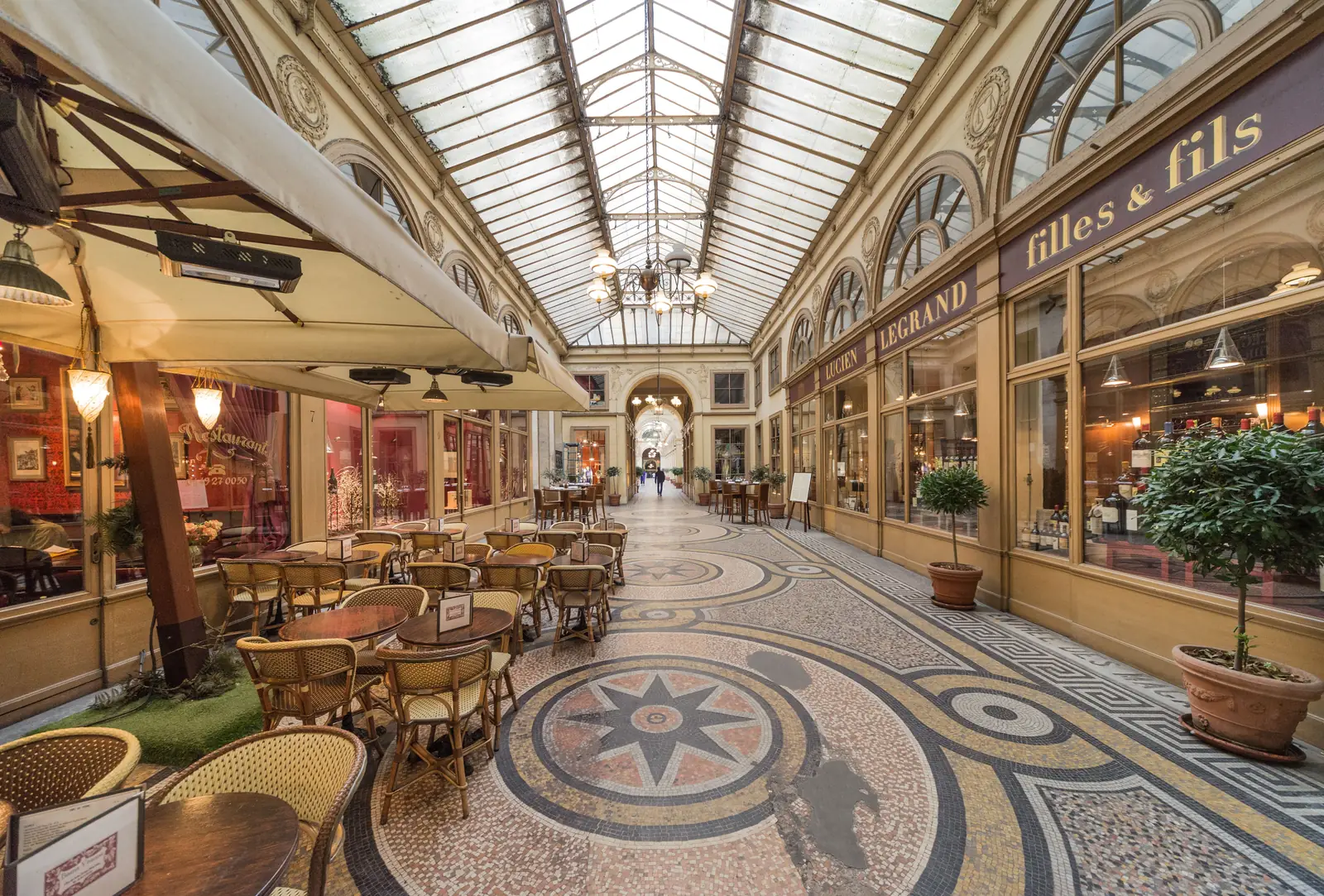 A glass roofed covered passage in Paris with a restaurant and mosaic floor