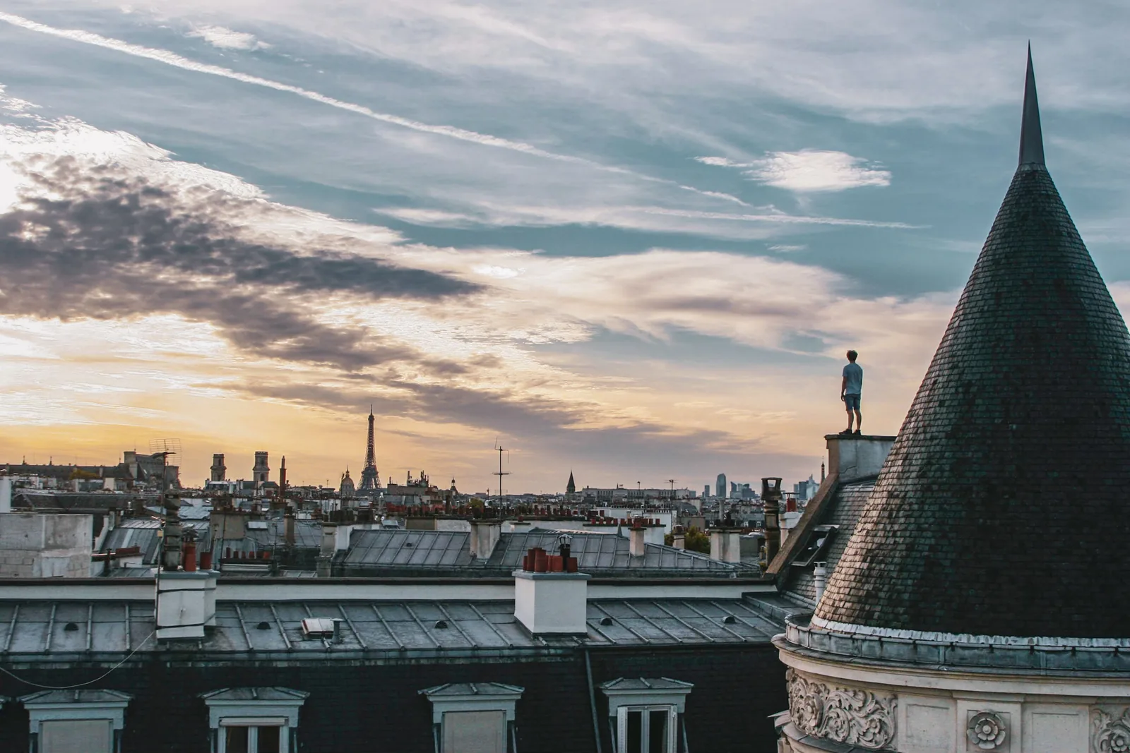 A person standing on a Paris rooftop looking out over the city at dusk