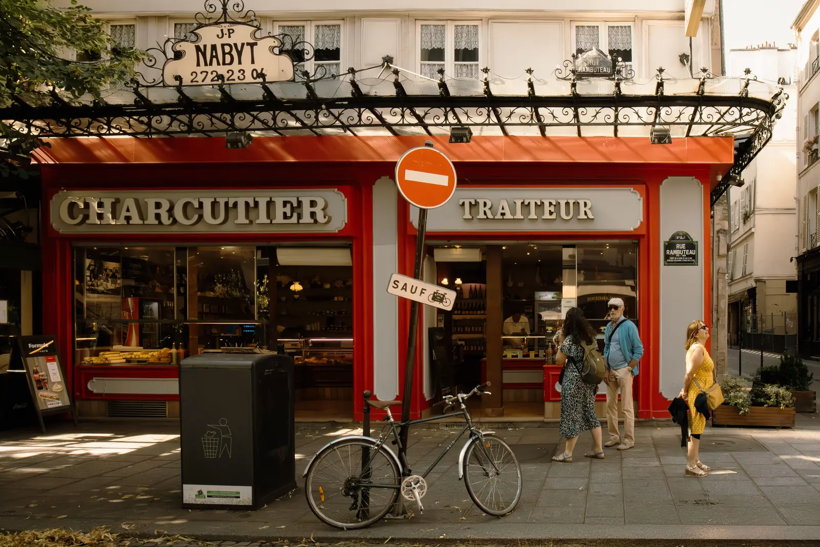 A red charcuterie shopfront with people talking outside on a Paris street