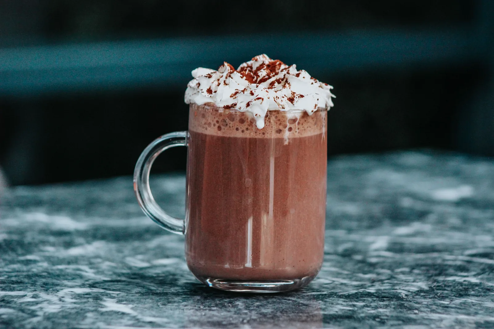 A glass mug of thick hot chocolate topped with whipped cream on a marble table