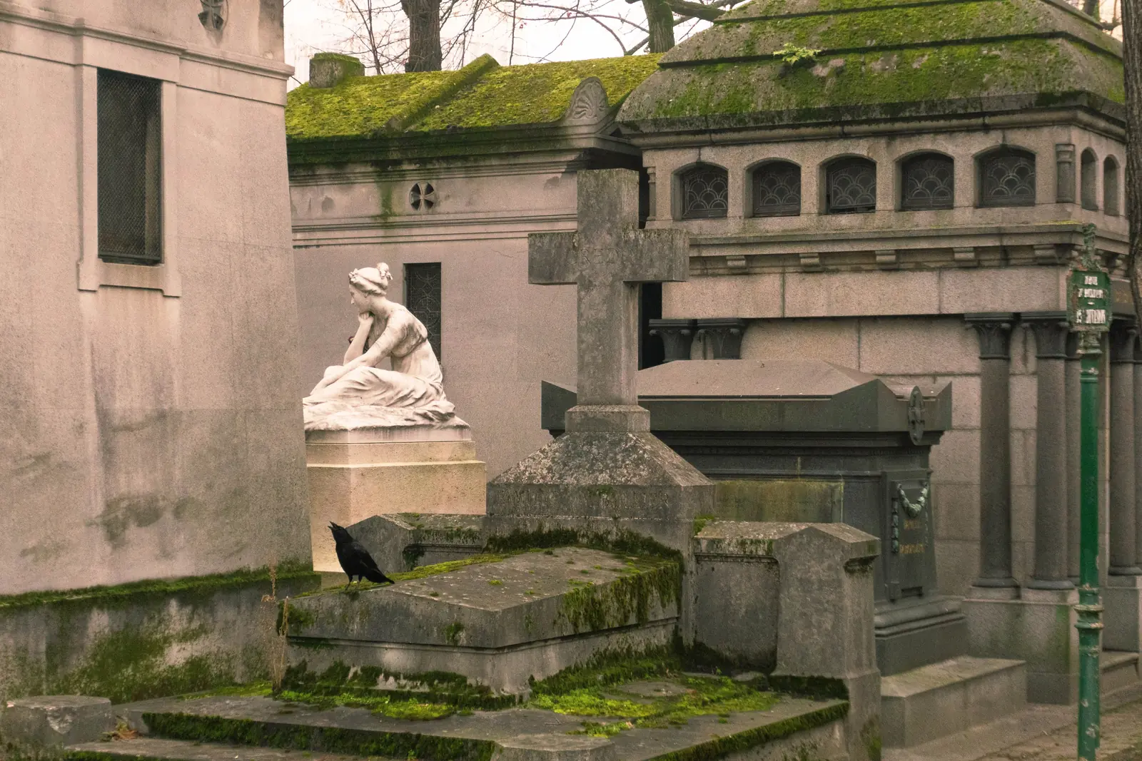 Moss covered tombs and a carved stone figure in Pere Lachaise cemetery in Paris