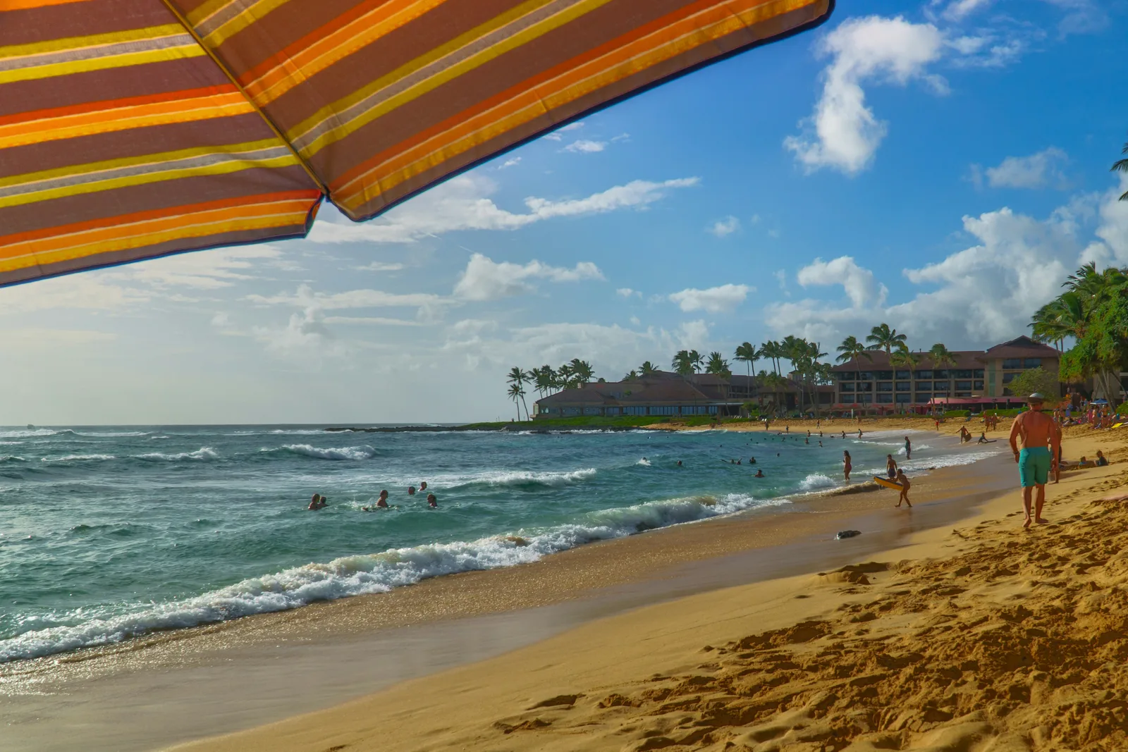 A striped beach umbrella and swimmers on a sunny stretch of sand