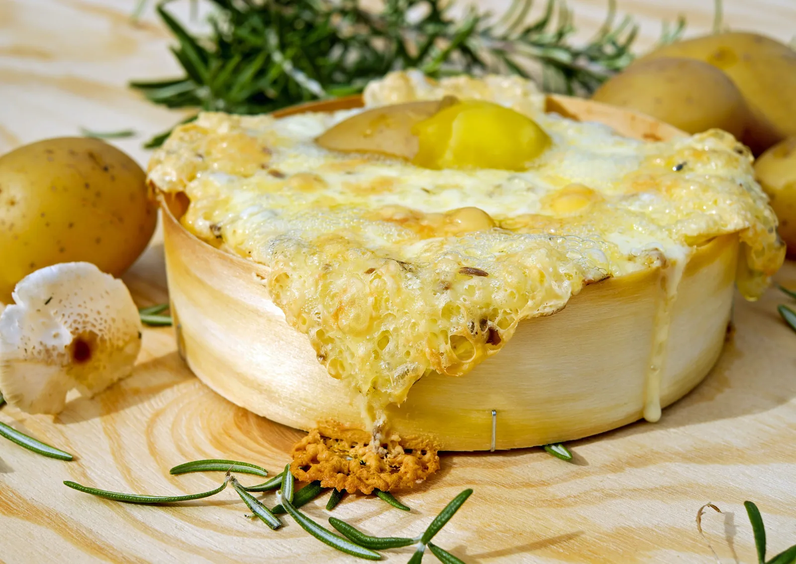 A whole round cheese melted over baby potatoes on a wooden board