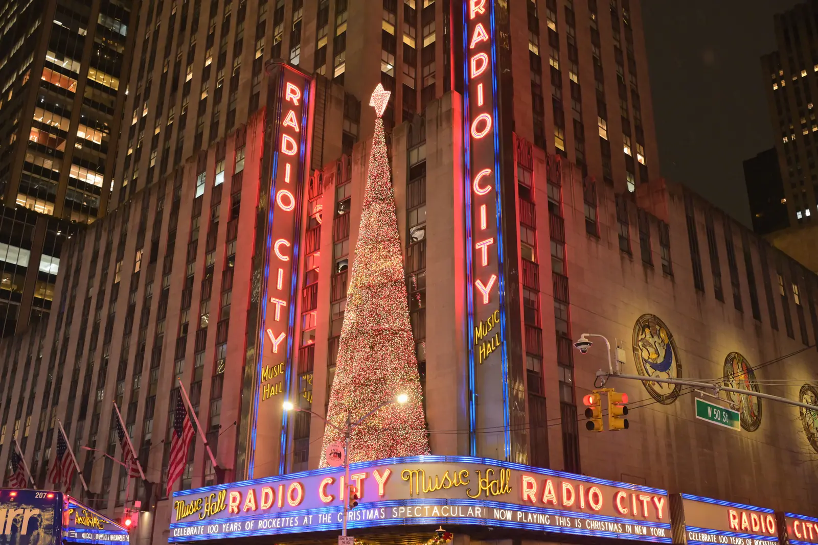 The Radio City Music Hall marquee lit in red beside a tall Christmas tree