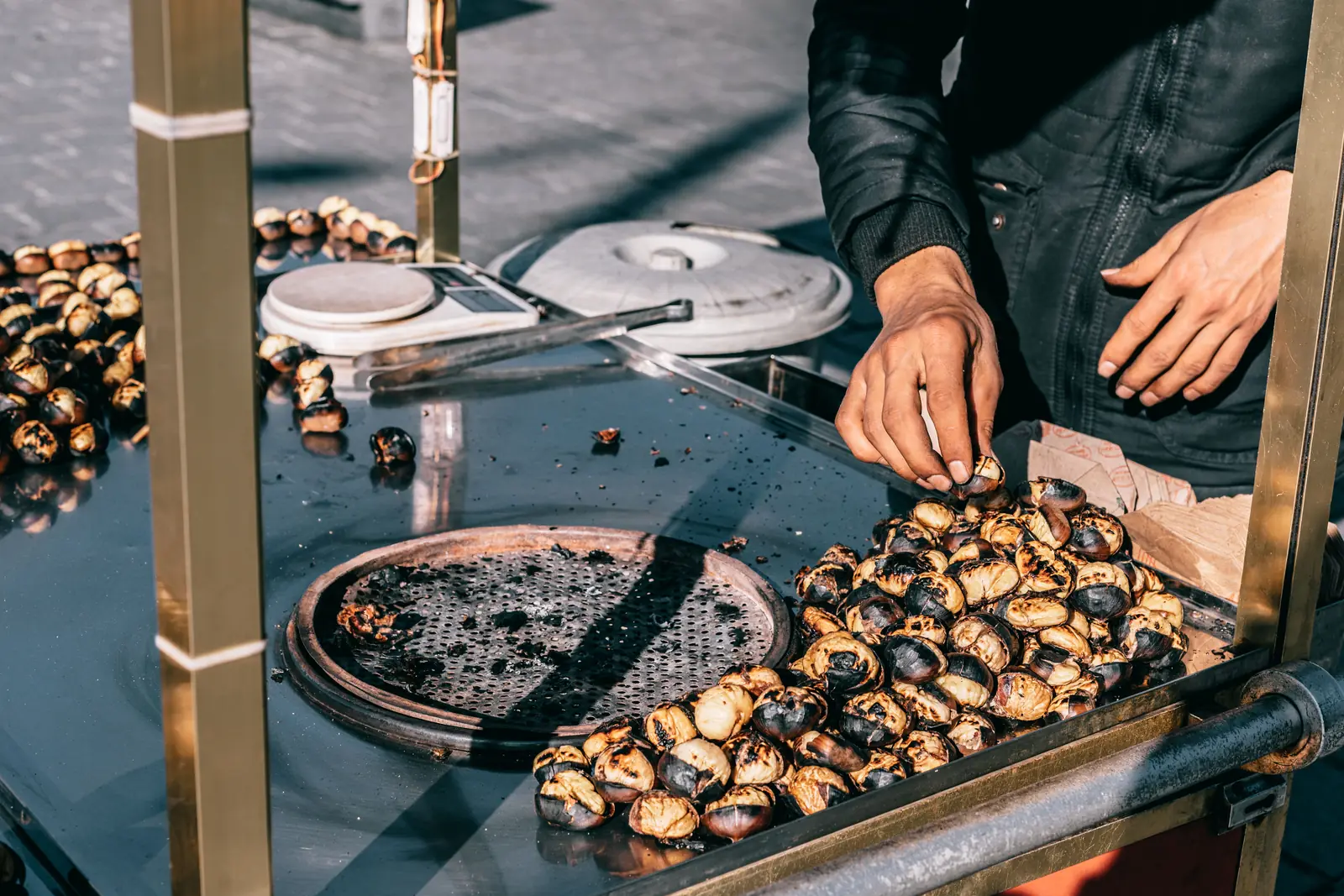 A vendor turning roasted chestnuts on a street grill