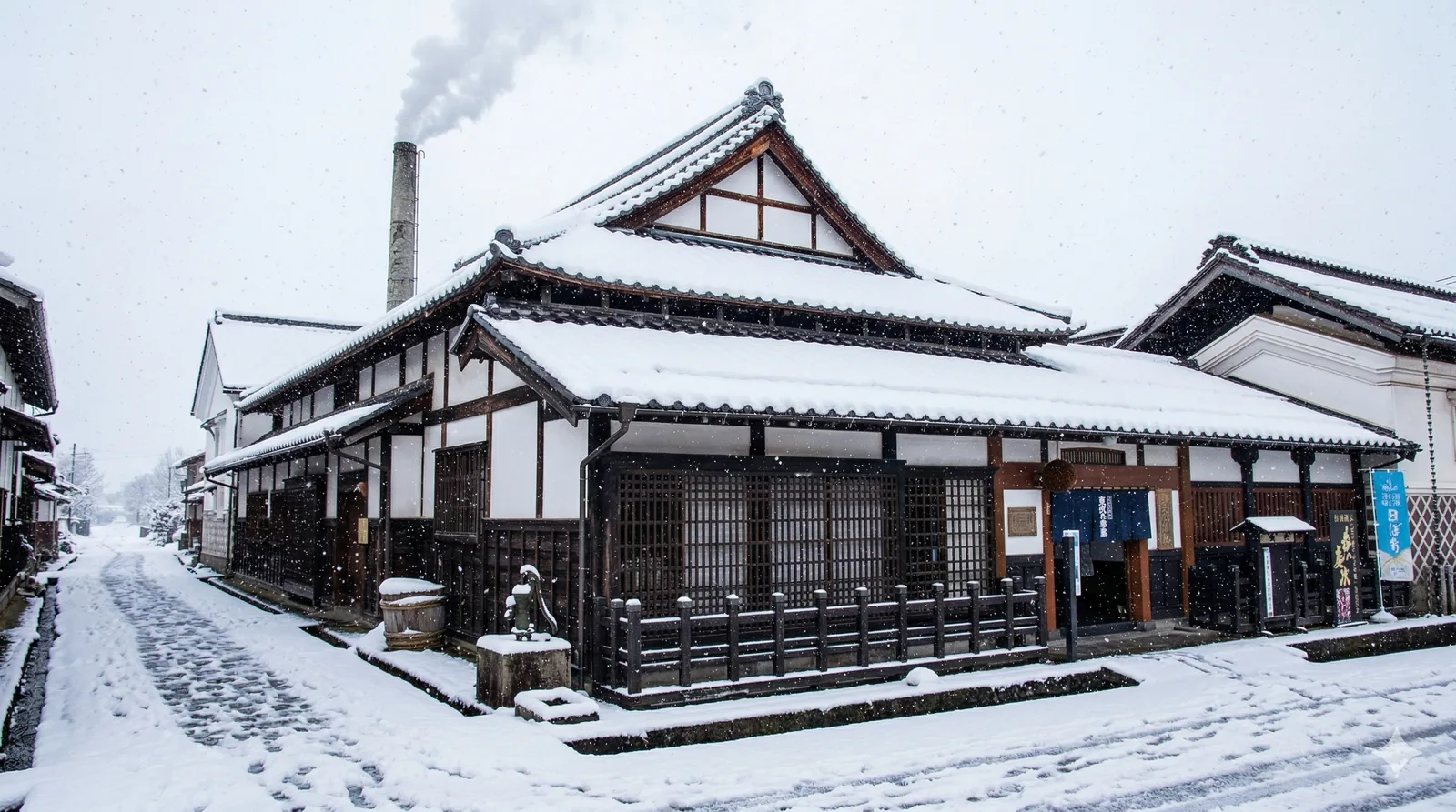 A traditional sake brewery in the snow with steam rising from the chimney