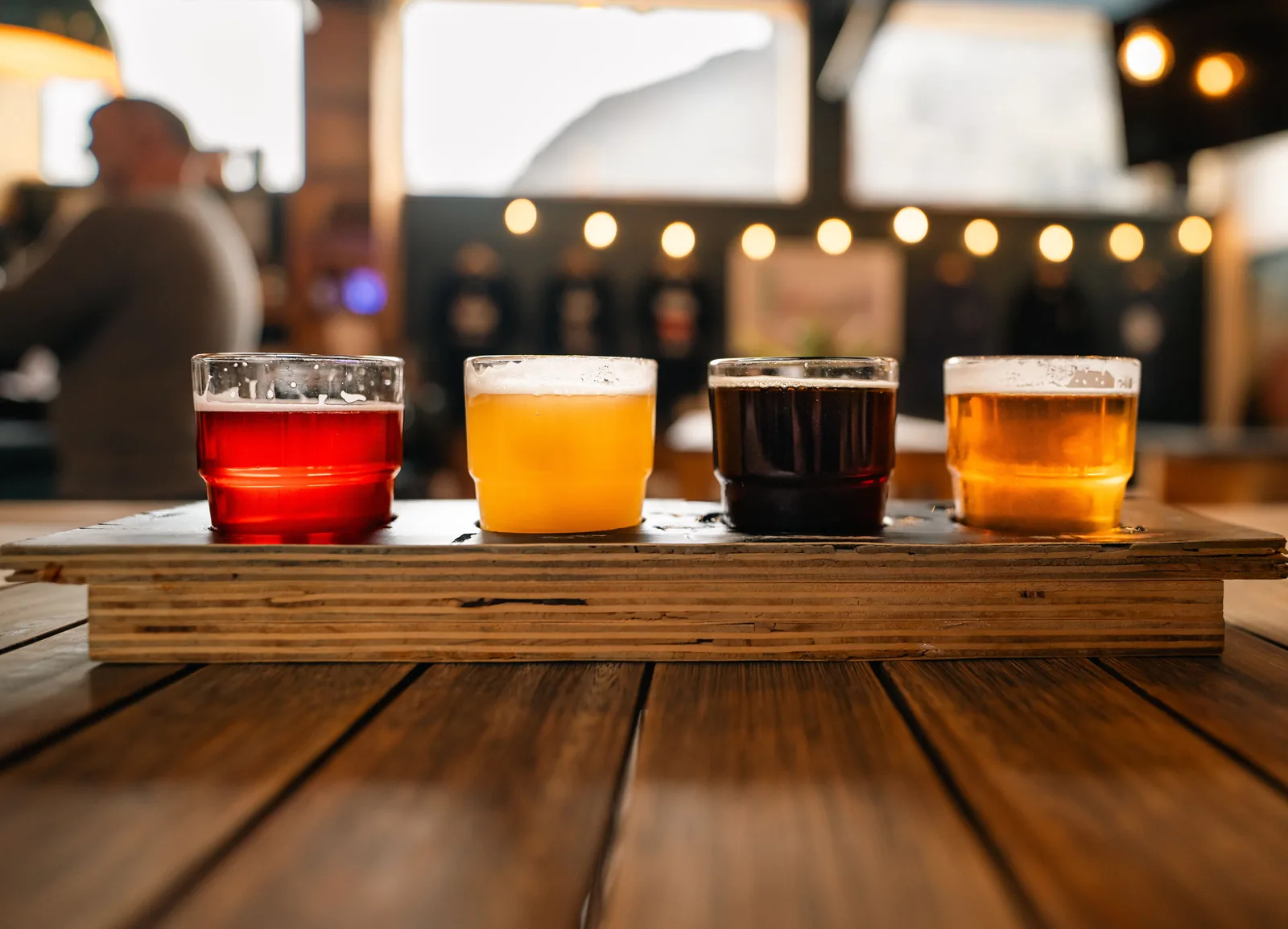 A flight of four beers lined up on a wooden table in a brewery taproom