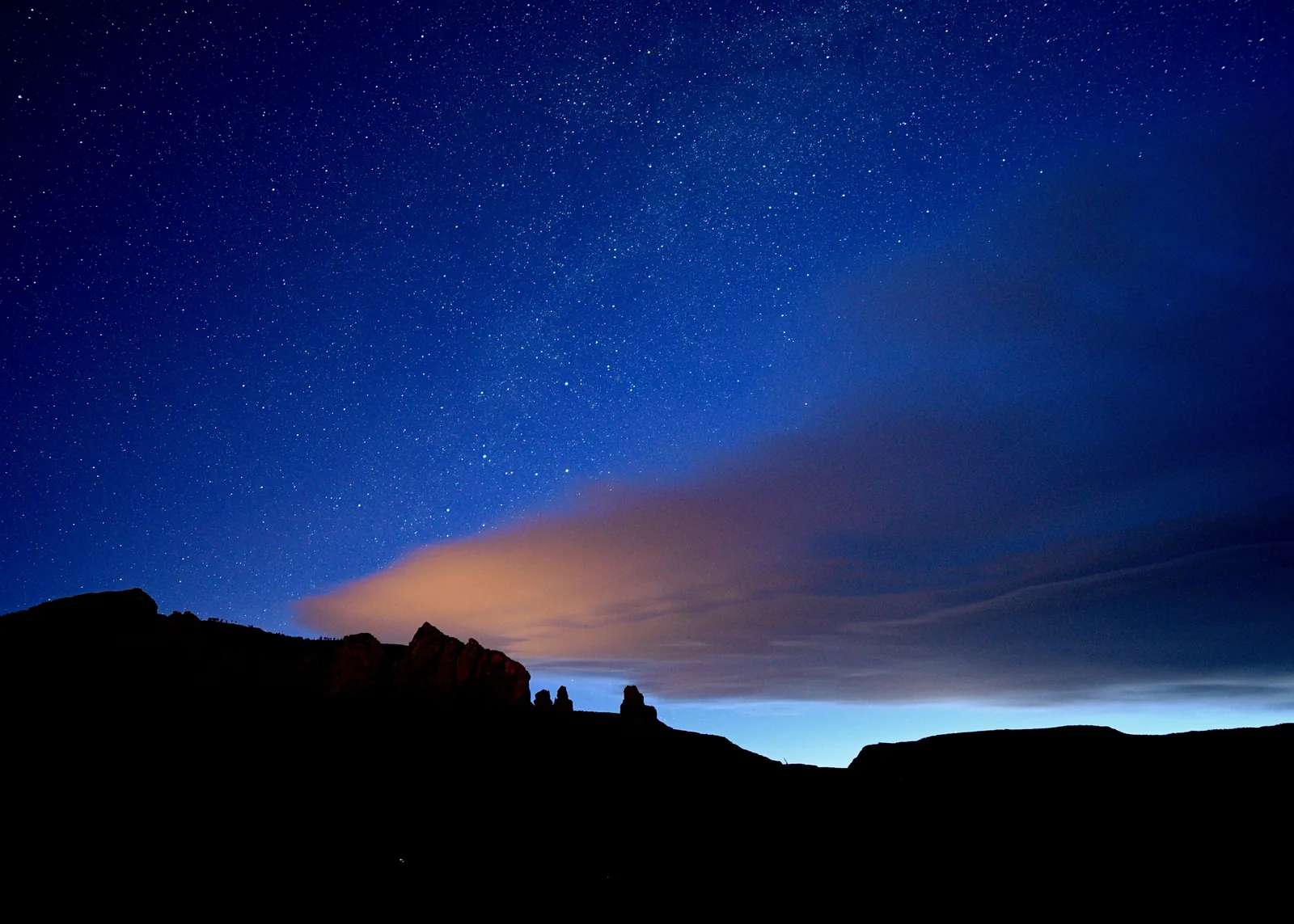 A starry night sky above a dark mountain silhouette