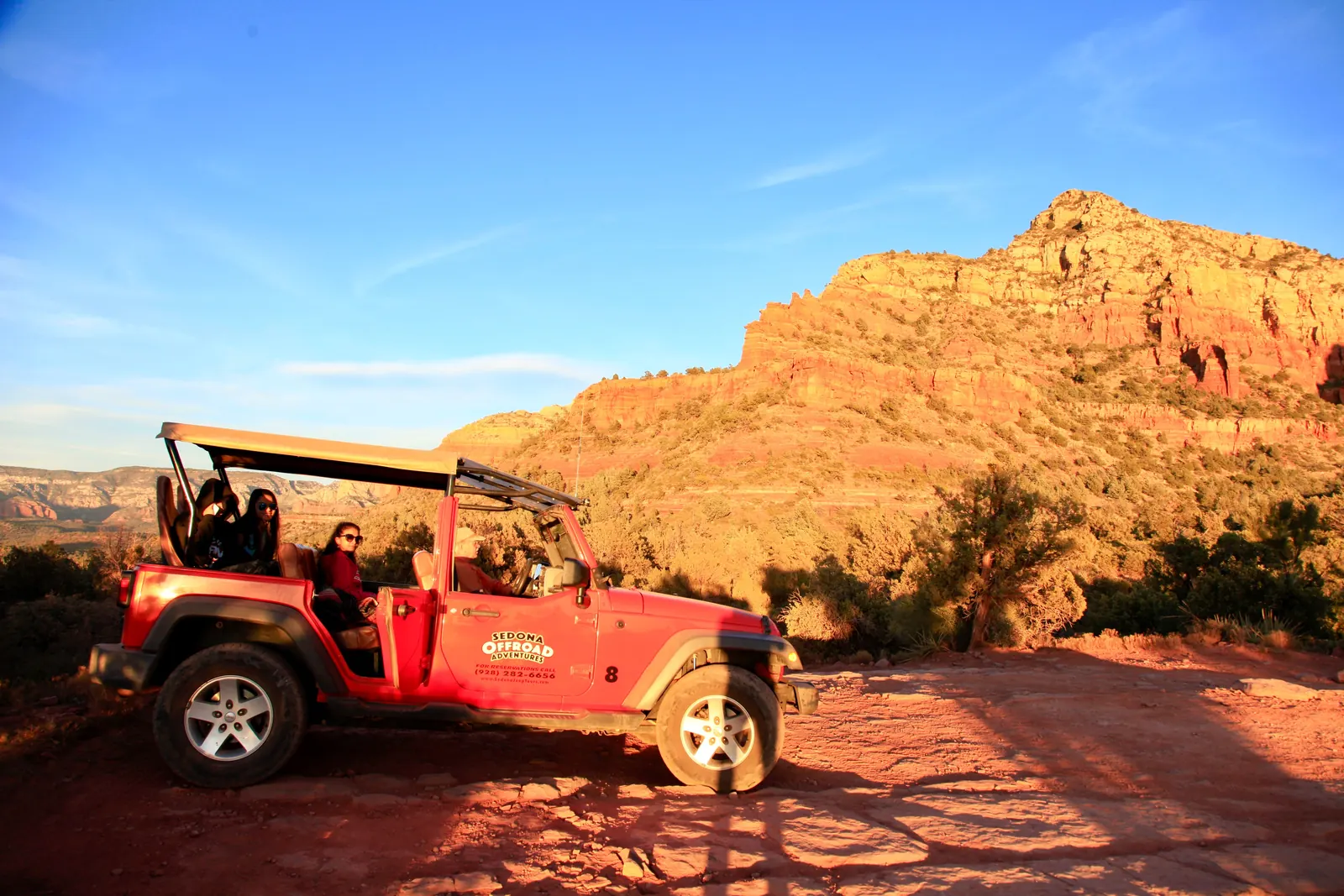An open top tour jeep on a red rock trail at golden hour
