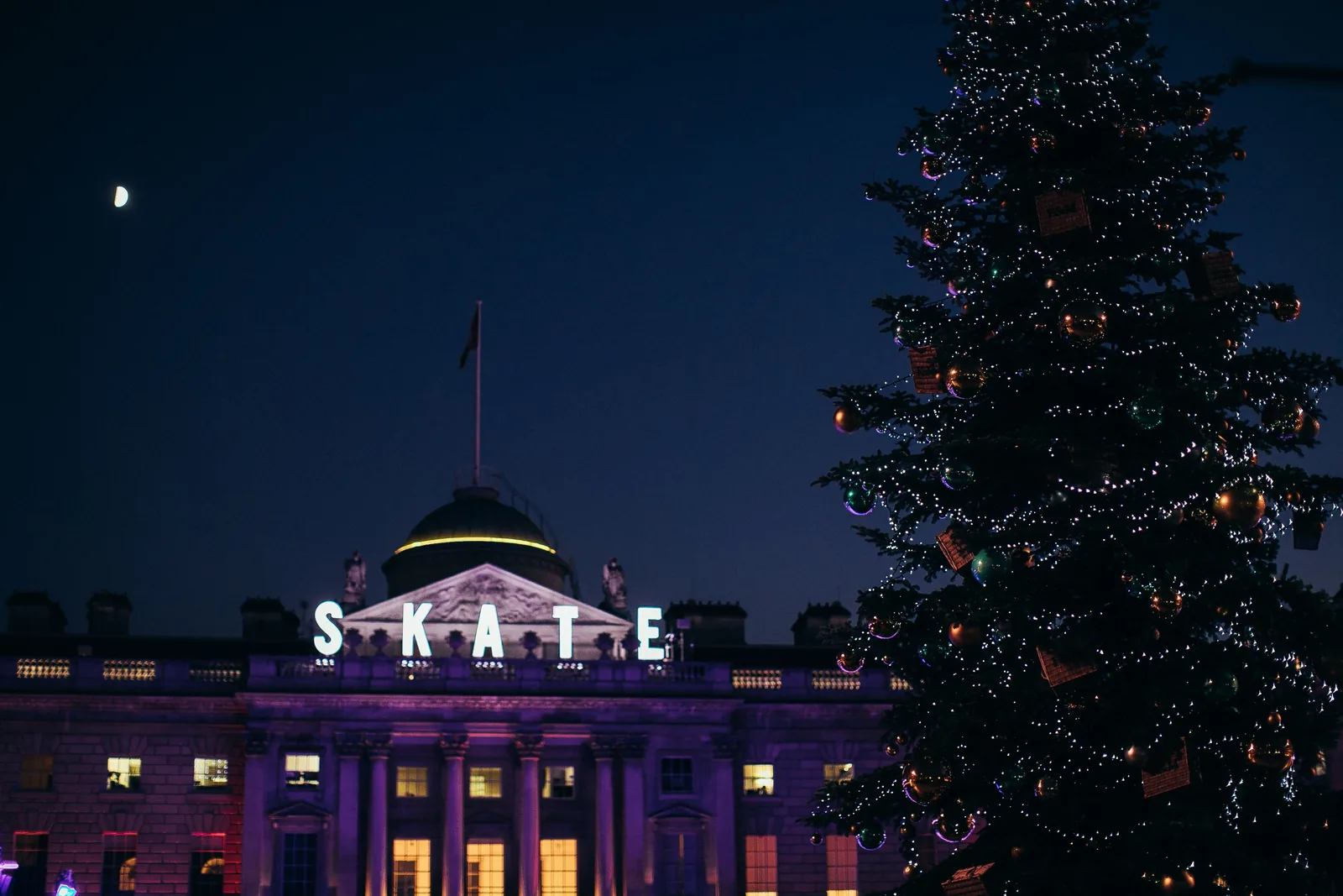 The SKATE sign lit up above Somerset House with a Christmas tree beside it