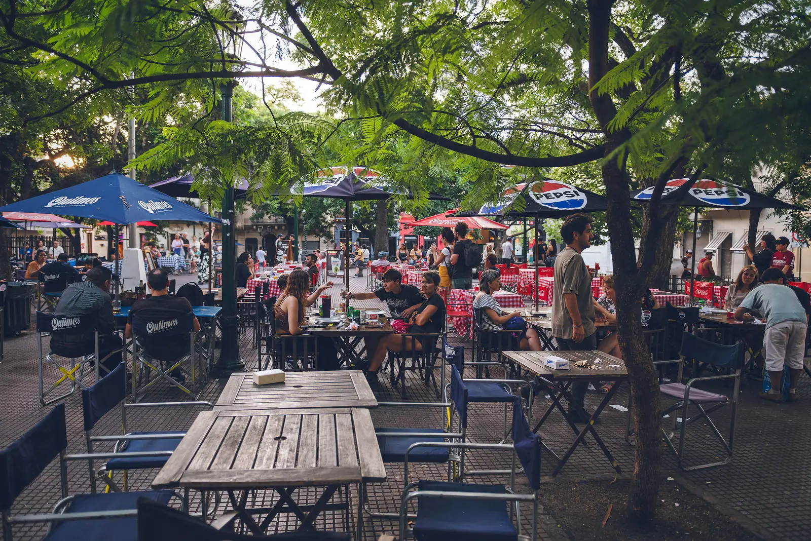 Cafe tables shaded by trees on a leafy sidewalk in Buenos Aires