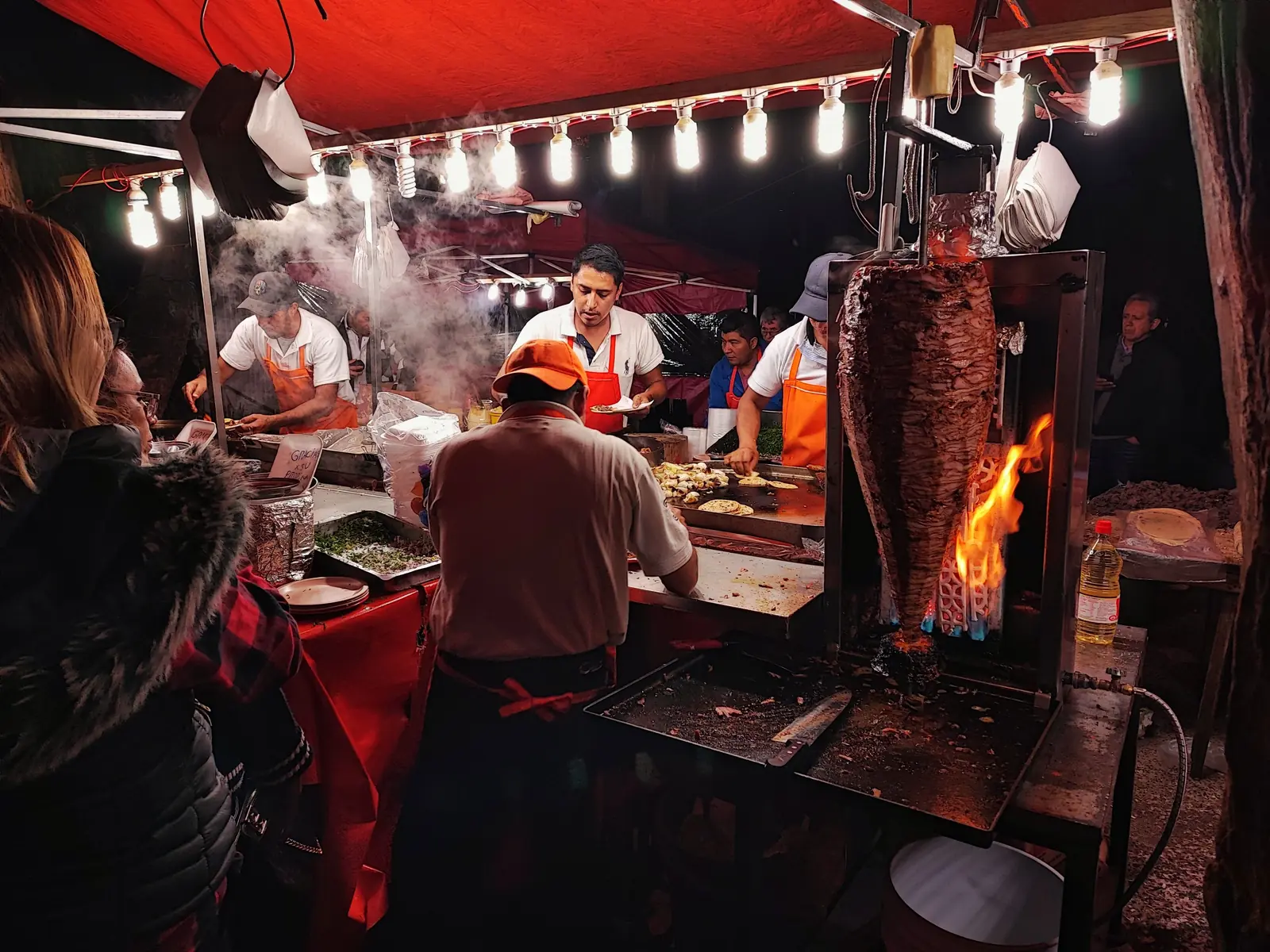 A busy taco stand carving al pastor under string lights at night in Mexico