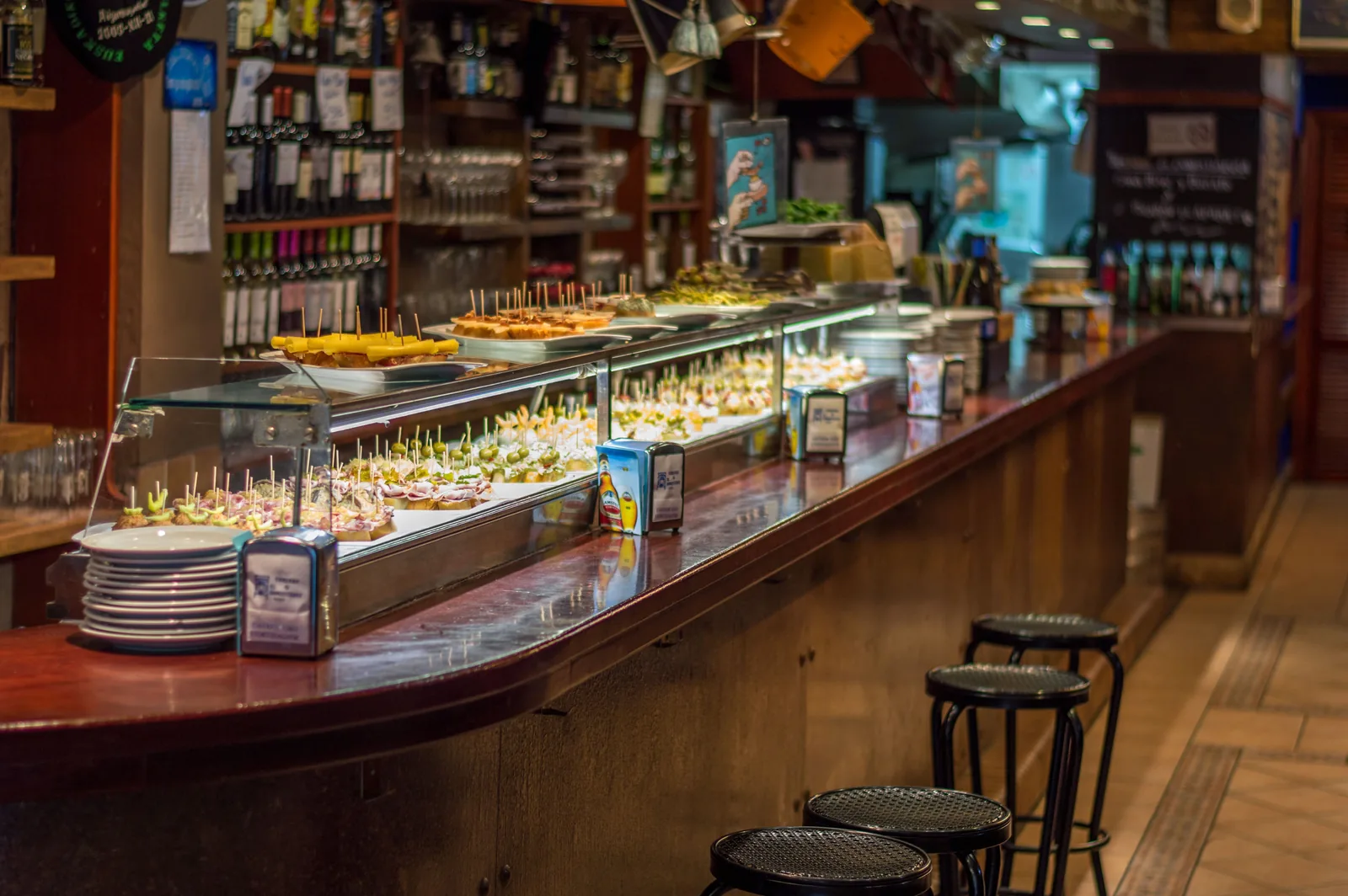 A bar counter lined with plates of pintxos and empty stools in Spain