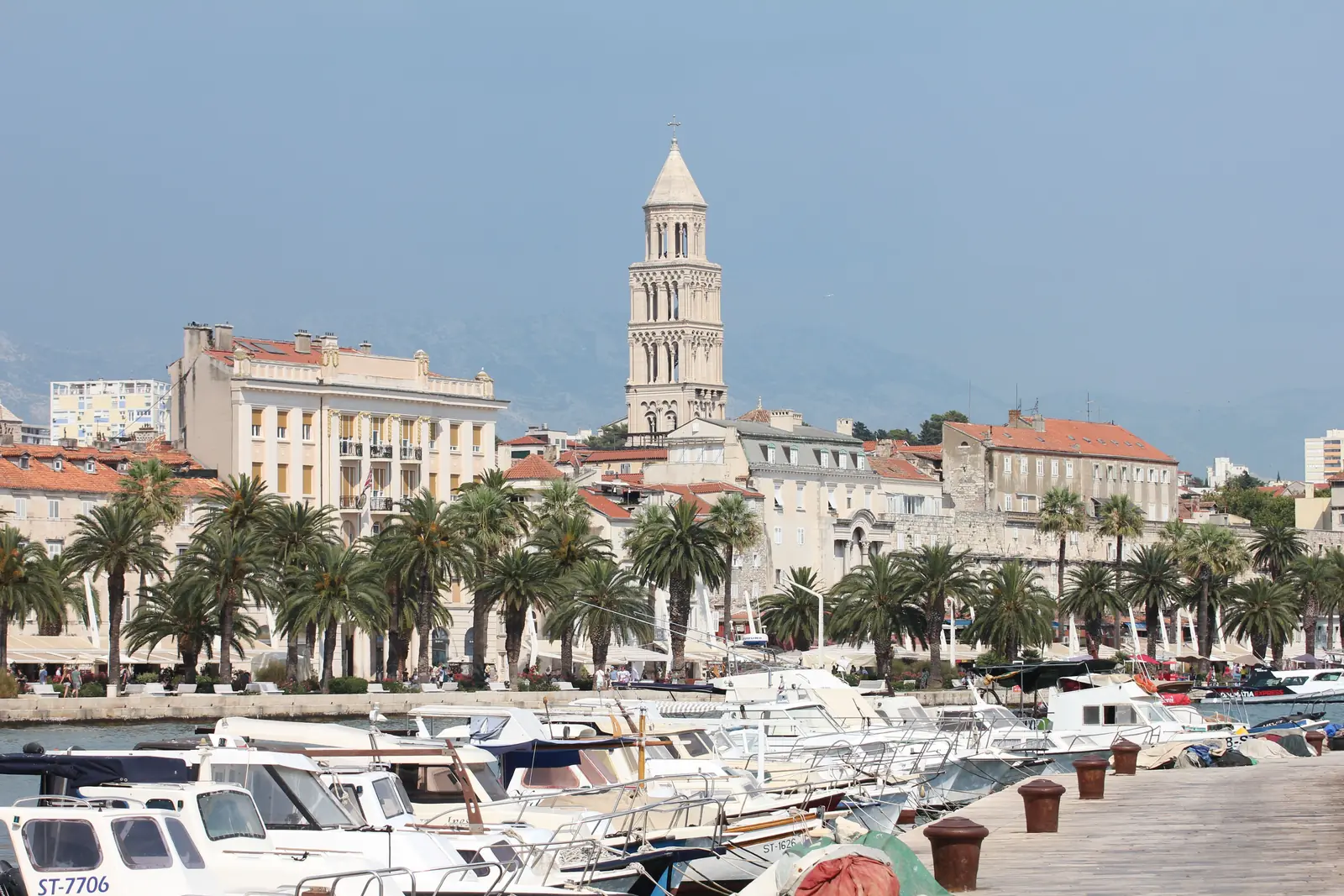 Palm trees and moored boats along the Split waterfront below the cathedral bell tower