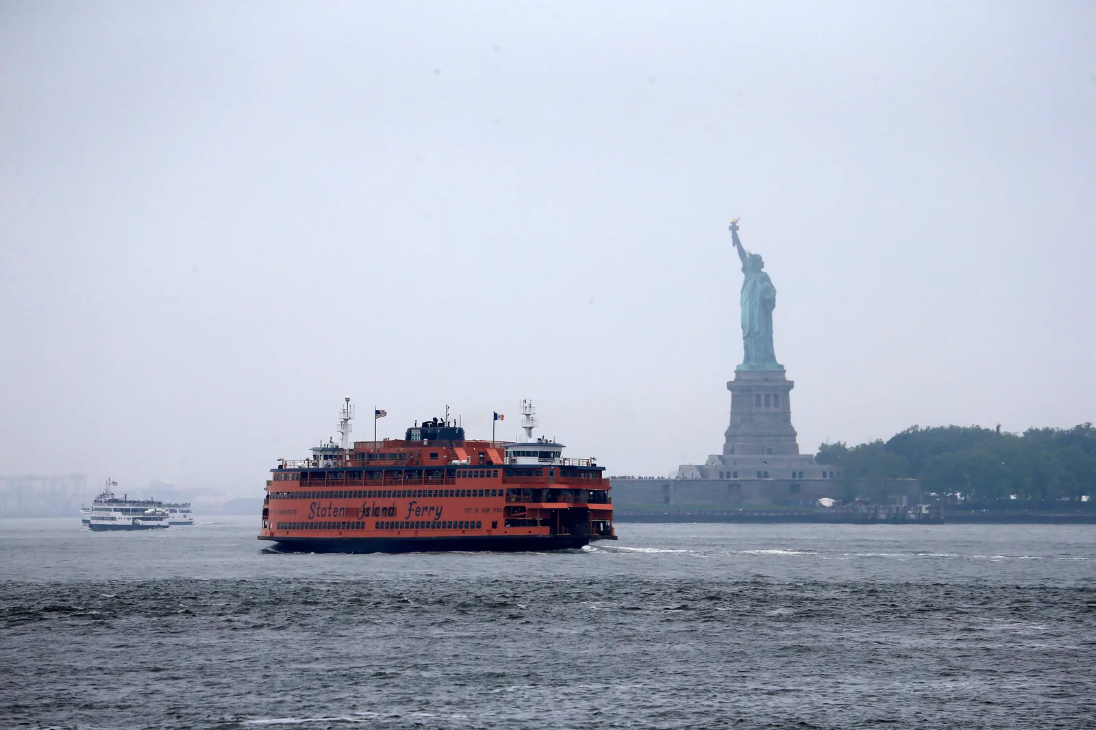 The orange Staten Island Ferry passing the Statue of Liberty