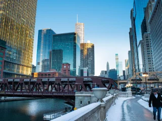 A person walking along a snowy path beside the Chicago River with the downtown skyline behind