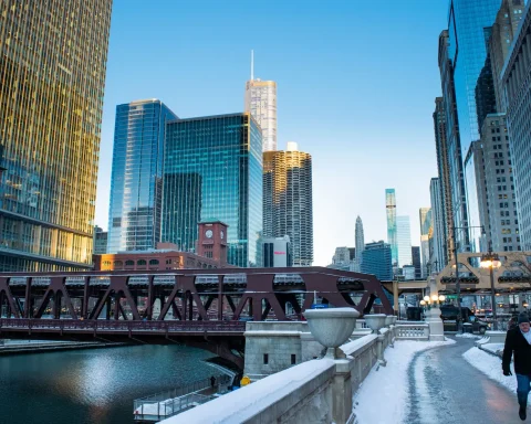 A person walking along a snowy path beside the Chicago River with the downtown skyline behind