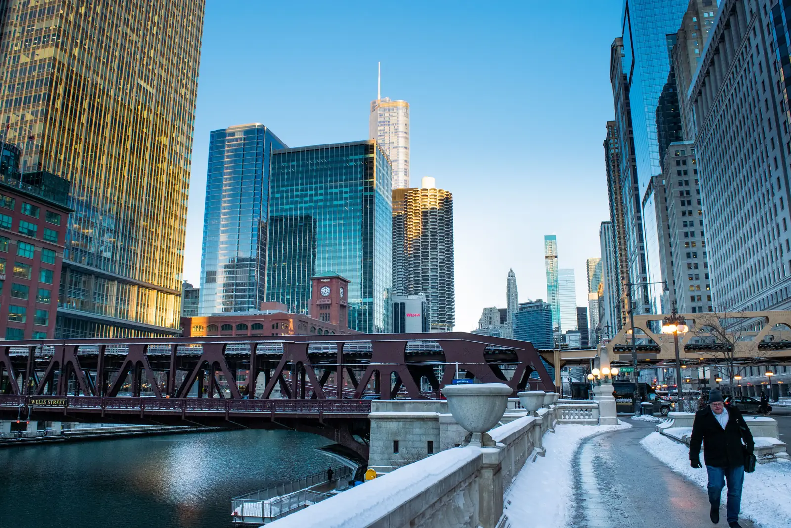 A person walking along a snowy path beside the Chicago River with the downtown skyline behind