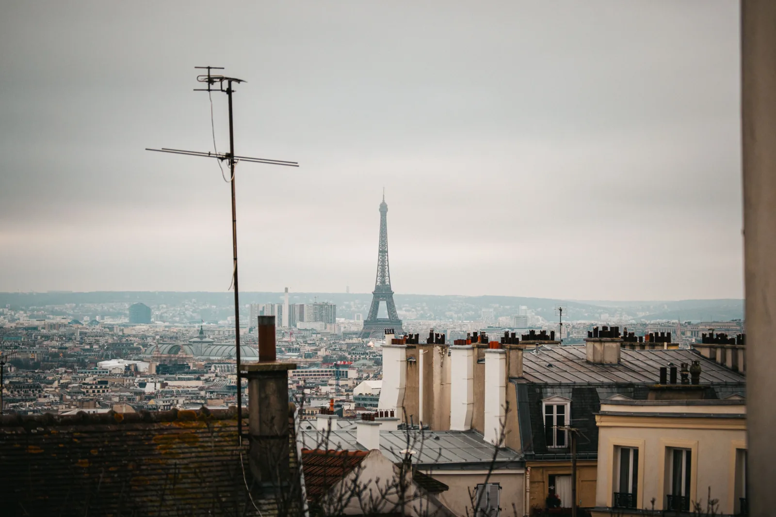 Paris rooftops and chimney pots under a soft grey winter sky with the Eiffel Tower in the distance