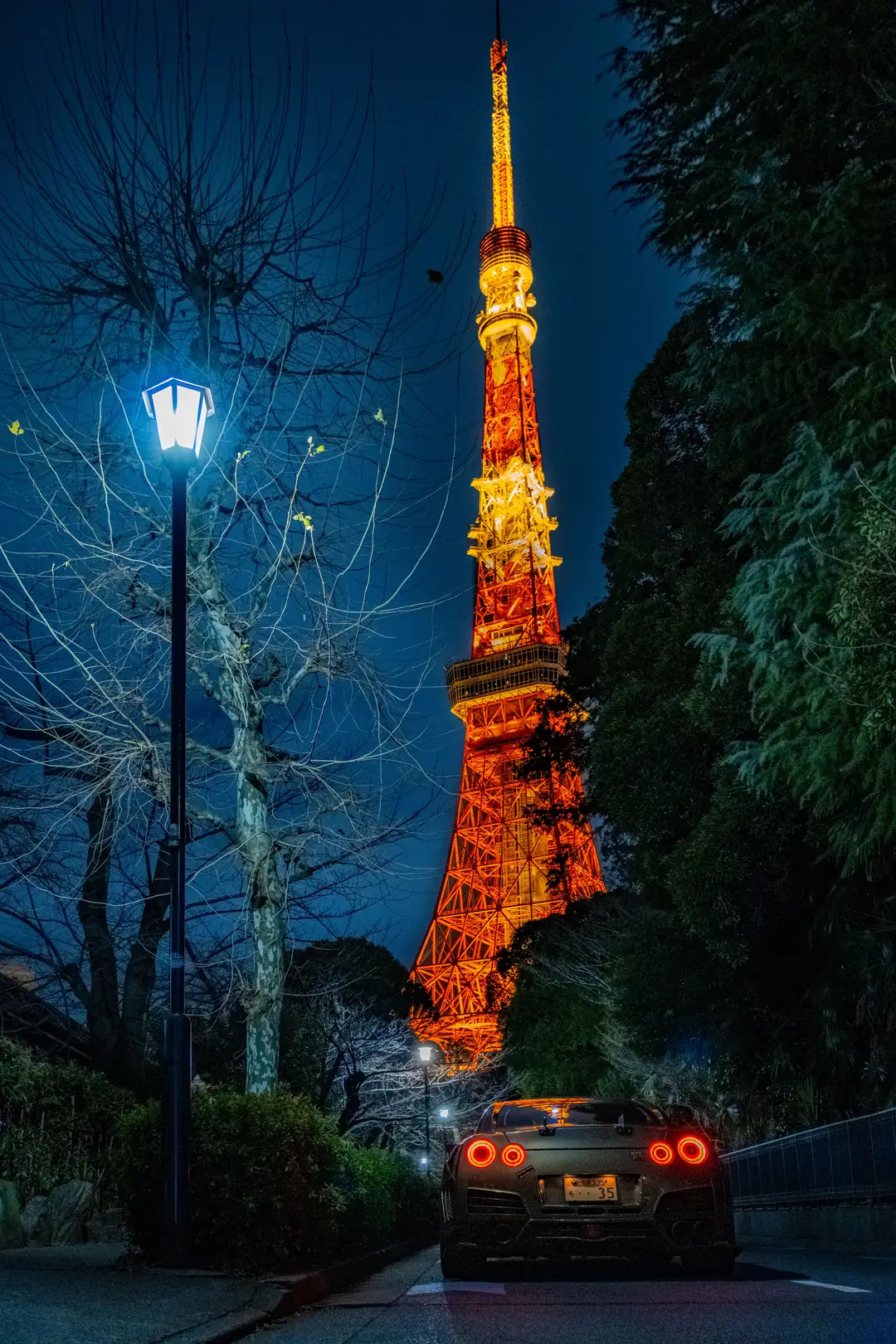 Tokyo Tower lit up at night behind bare winter trees