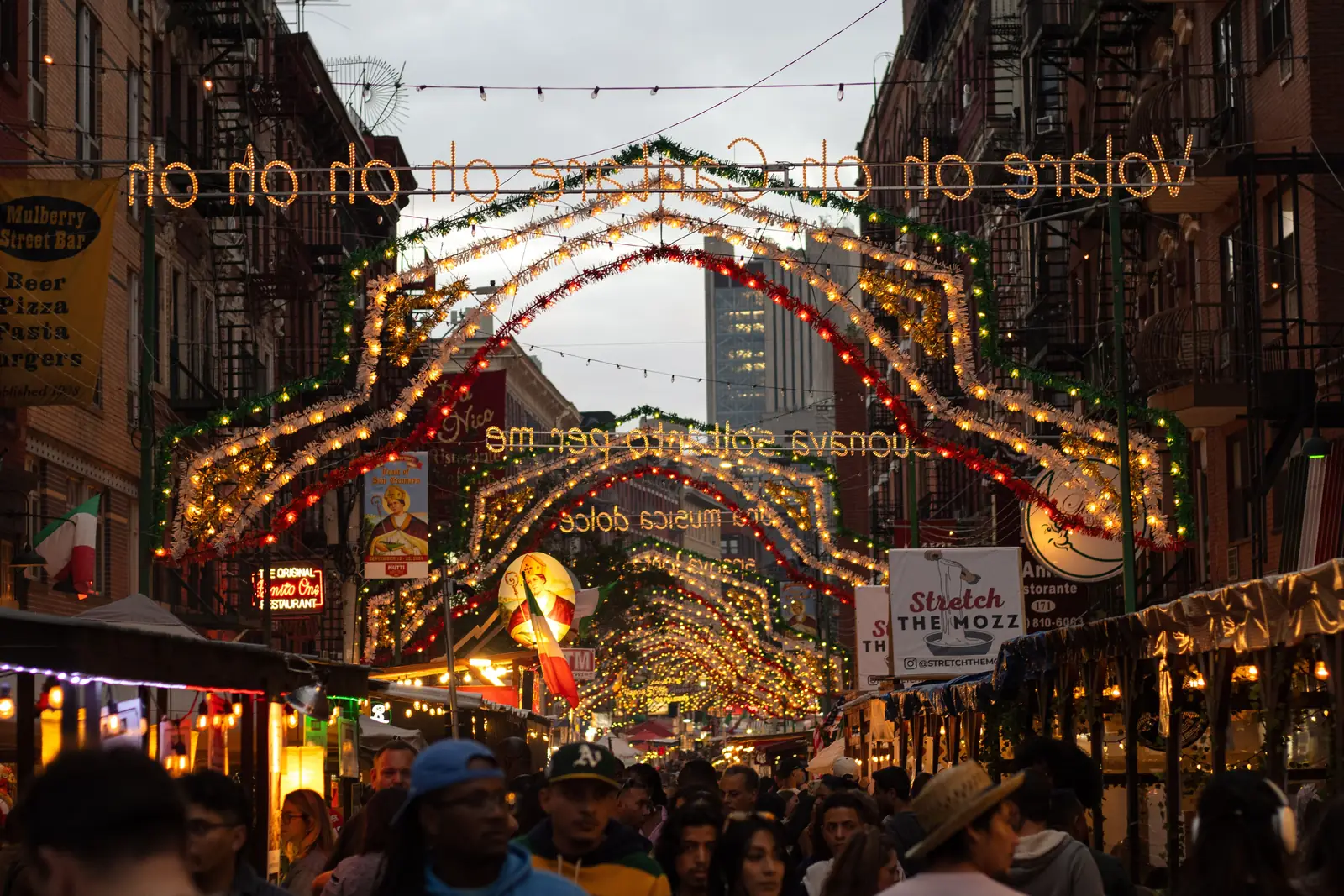 A holiday market stall lit up after dark with shoppers walking past