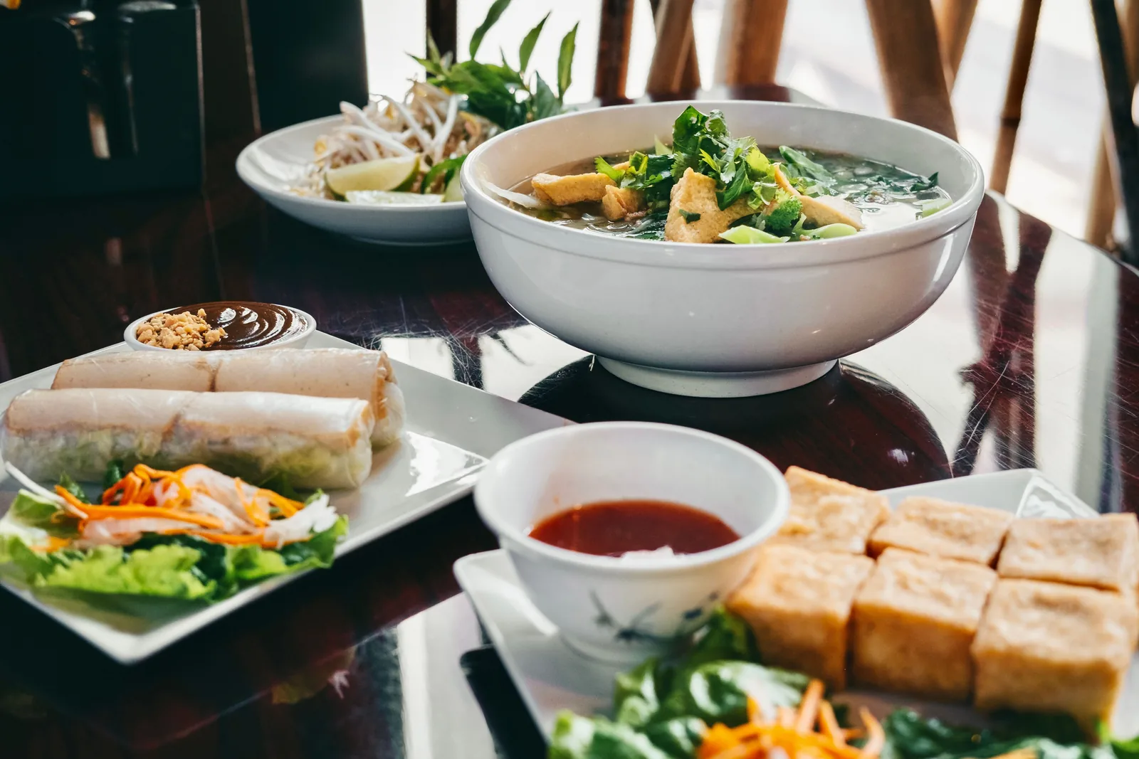 Bowls of pho, spring rolls and fried tofu spread across a restaurant table