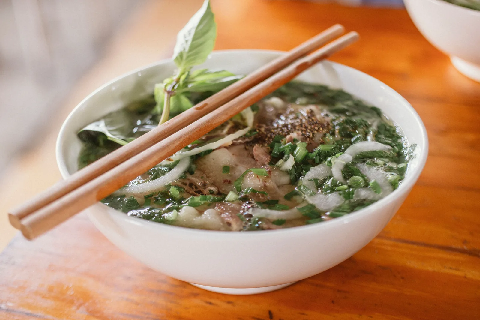 A bowl of pho with noodles, beef and fresh herbs