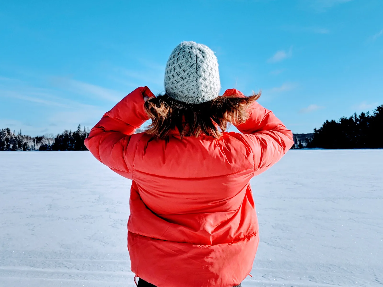 A person in a warm red puffer jacket looking out over an open snow field