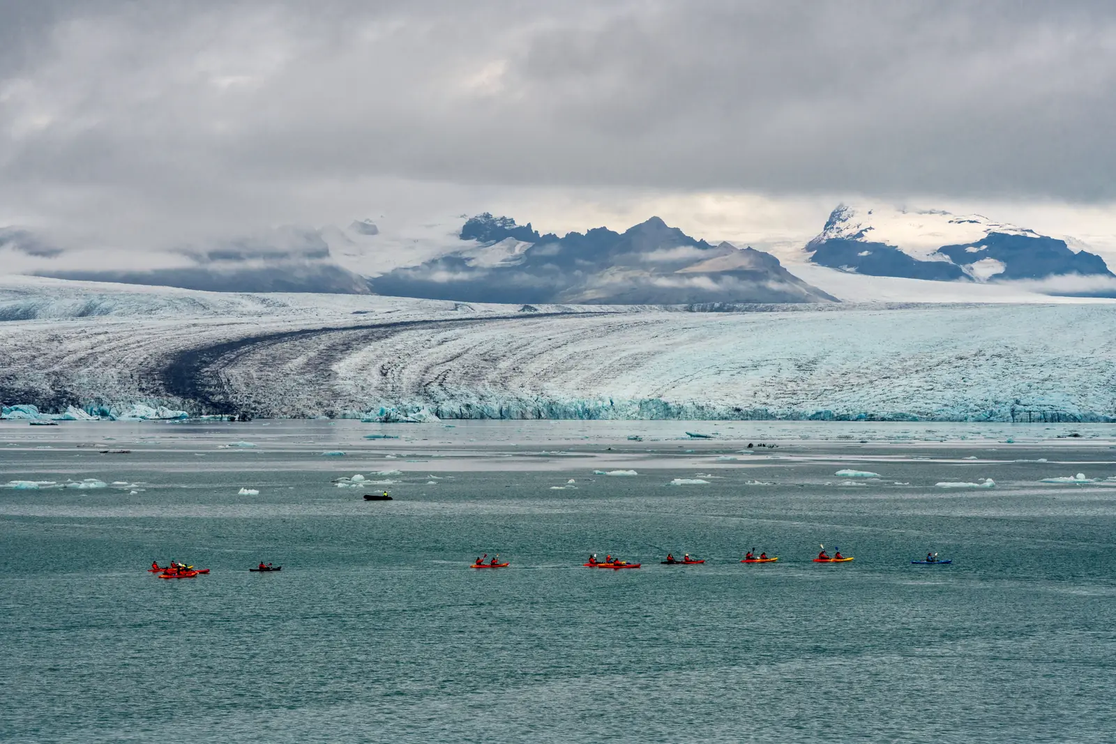 Kayakers paddling in a line in front of a wide glacier face