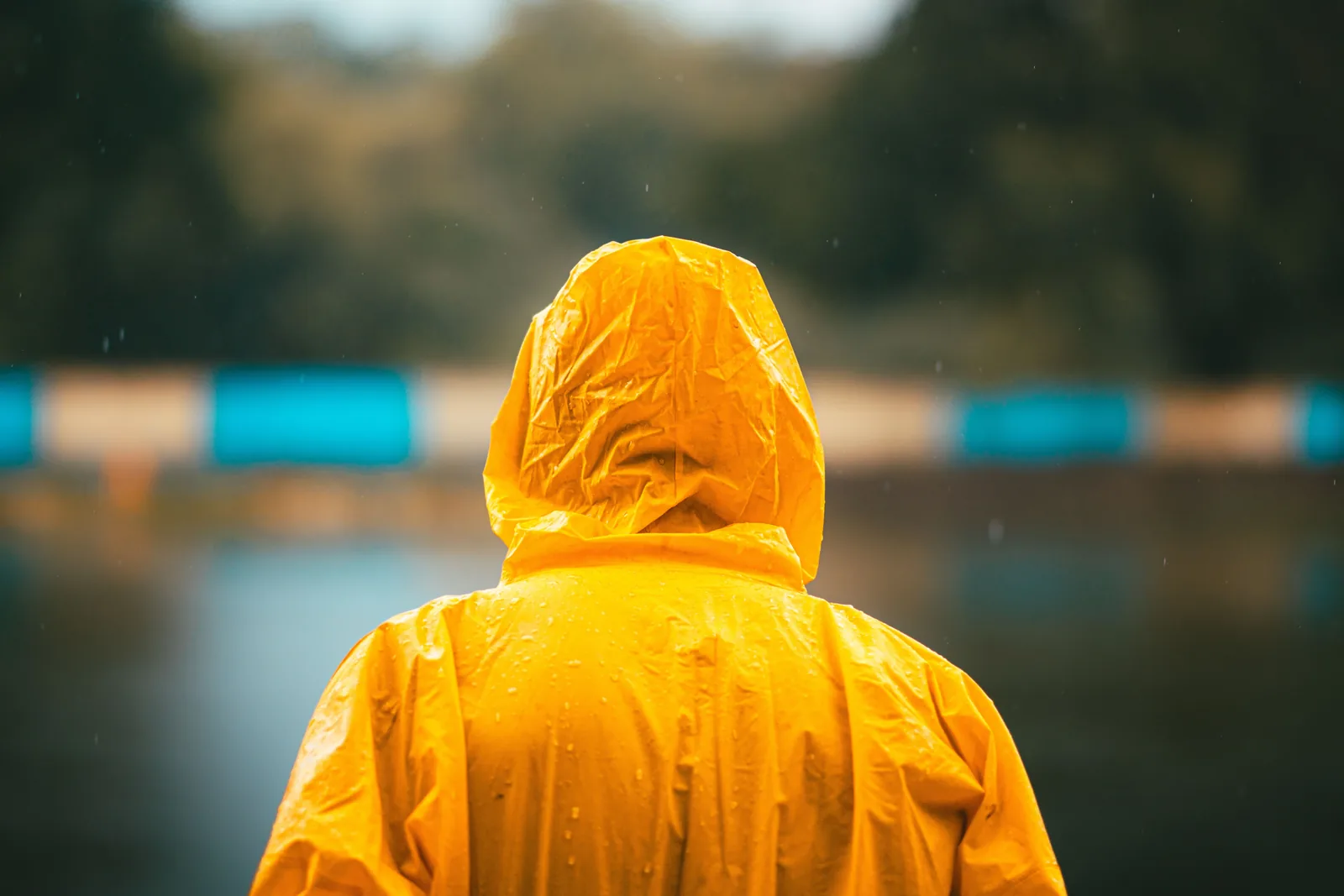 A person in a yellow waterproof rain jacket facing a misty lake